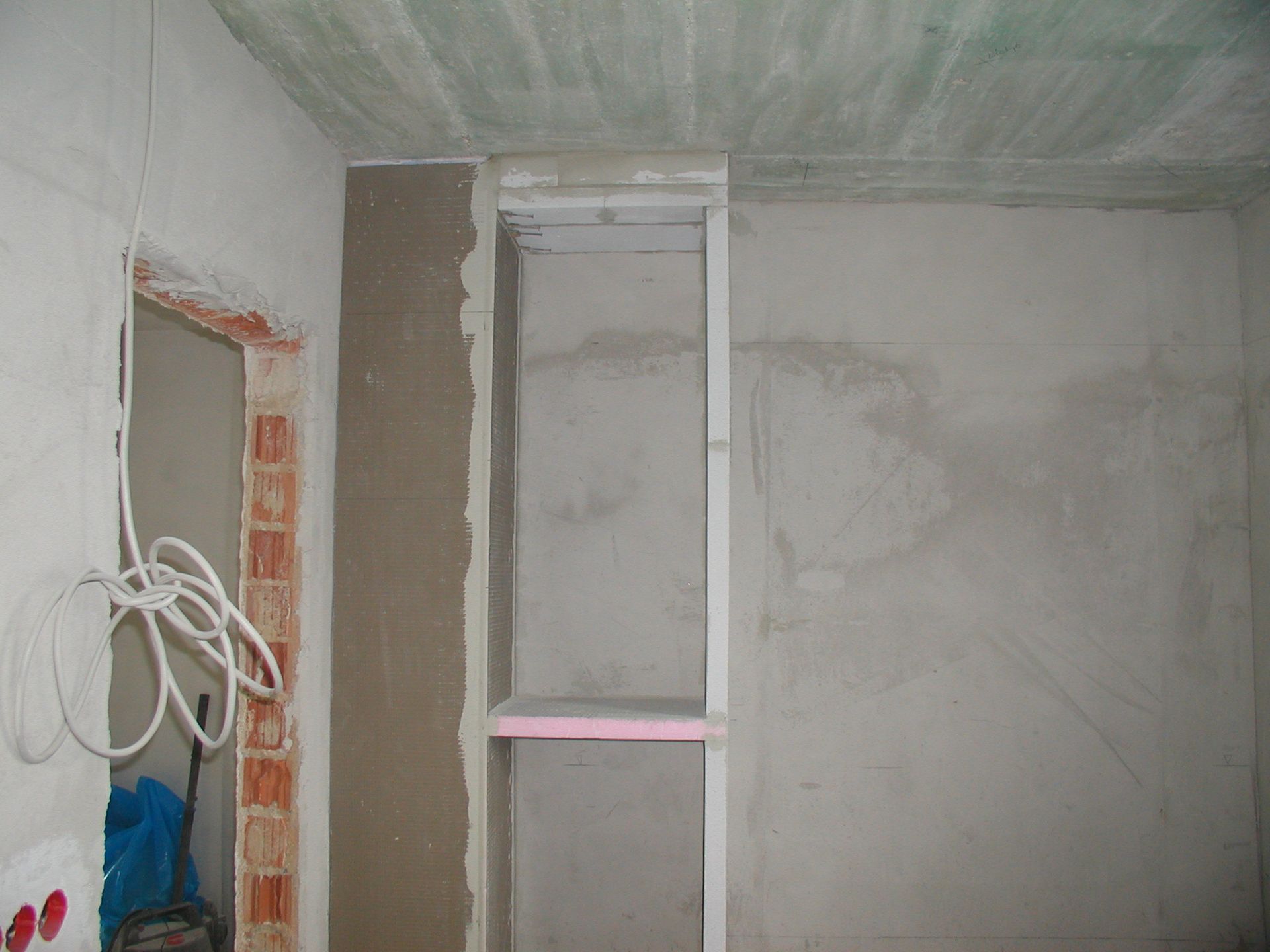 Innenausbau im Gange; graue Wände mit eingebauter Nische, freiliegender Verkabelung und einem Türrahmen aus Ziegeln.