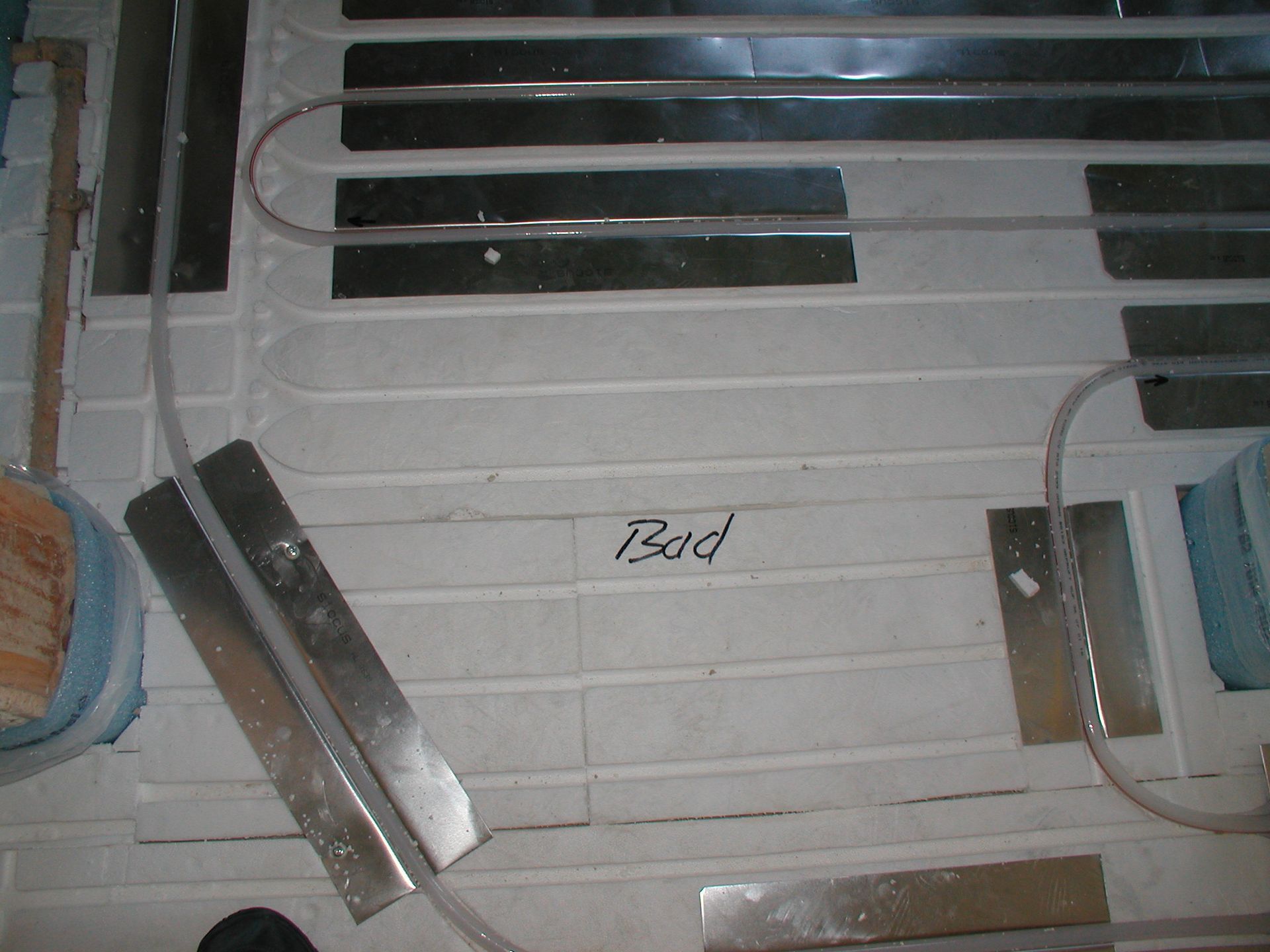 Fußbodenheizung im Bau; Rohre, Metallstreifen und Isolierung sichtbar. Aufschrift „Bod“.