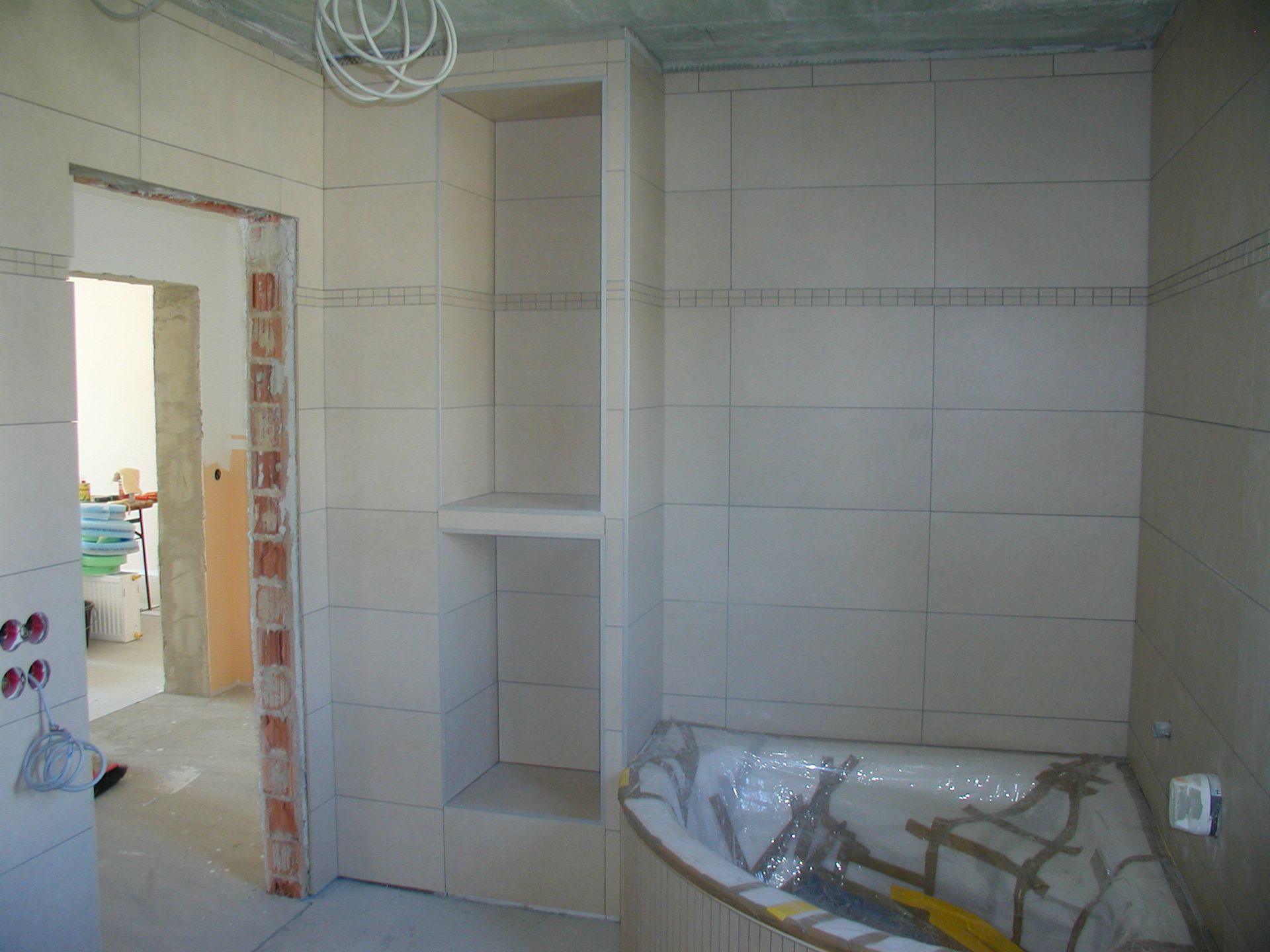 Im Bau befindliches Badezimmer mit gefliesten Wänden, Einbauregal und Badewanne.