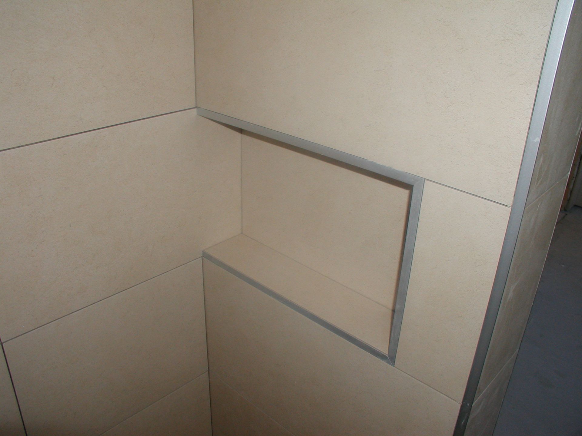 Eckige Duschnische, beige Wände, rechteckiges Regal mit Metallverkleidung.