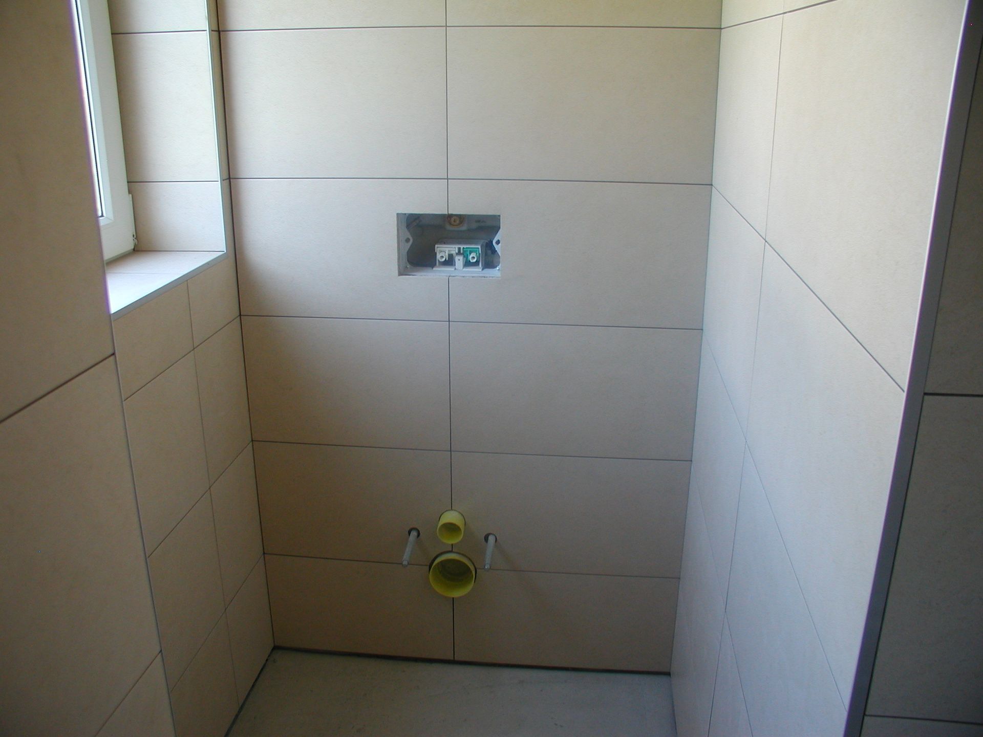 Badezimmer im Bau, mit installierten Wandpaneelen. Spülventil und Rohrleitungen sichtbar.