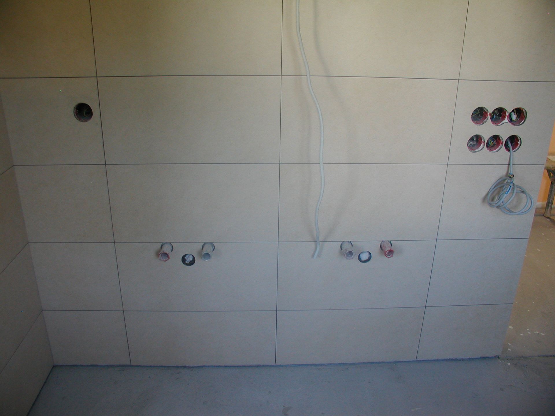 Weiß geflieste Wand mit Elektro- und Sanitärinstallationen während der Bauarbeiten.
