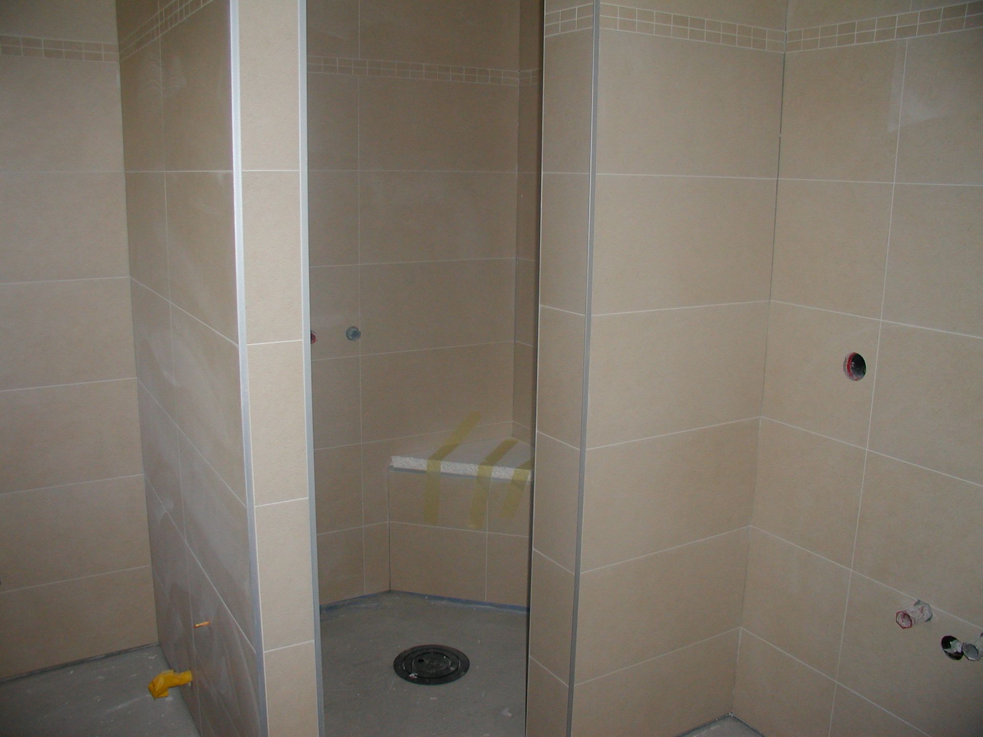 Gefliester Duschraum im Bau mit drei separaten Kabinen. Hellbraune Fliesen und grauer Boden.