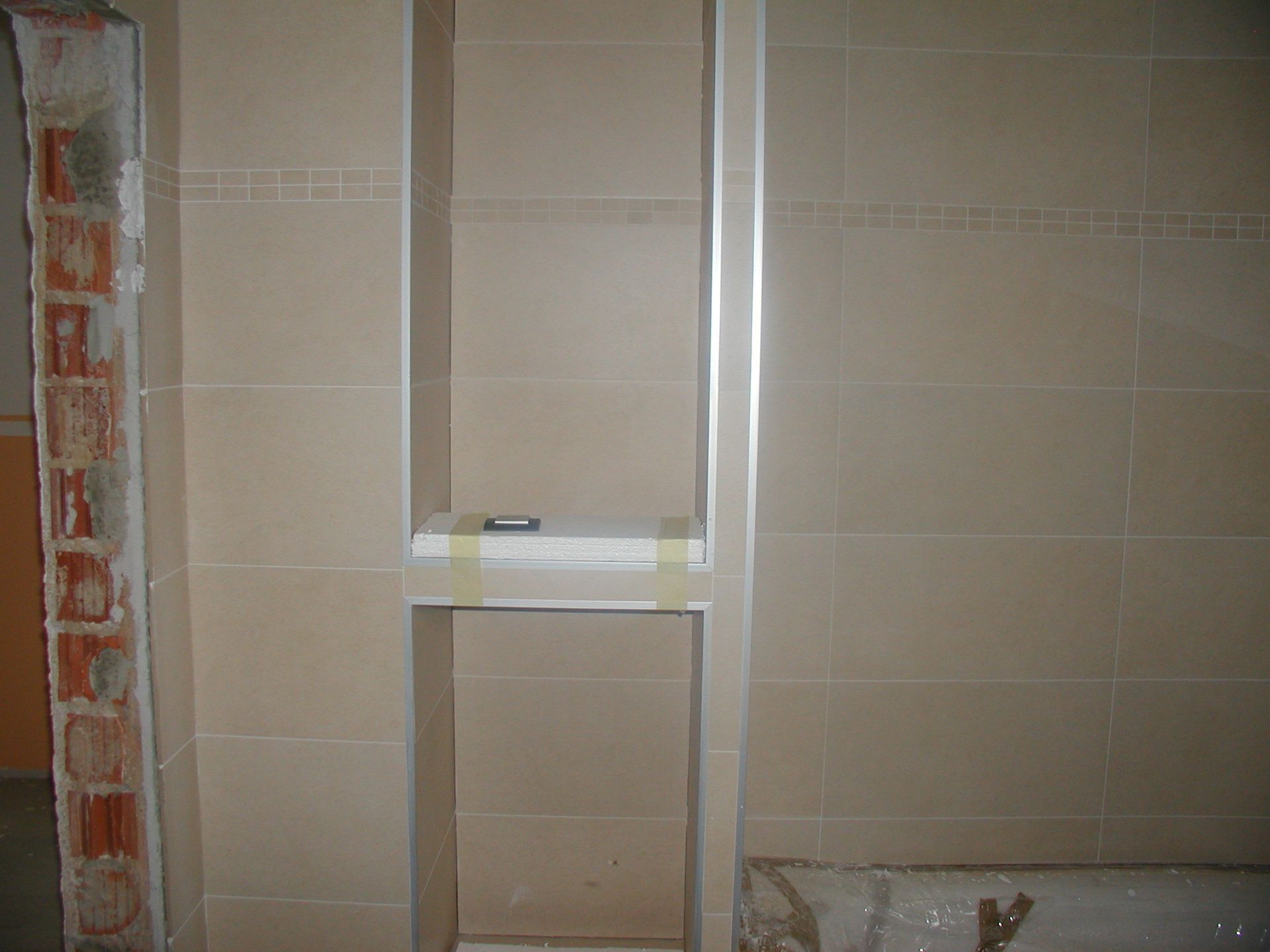 Beige geflieste Nische in einer Wand, mit einer teilweise freiliegenden Ziegelwand auf der linken Seite.