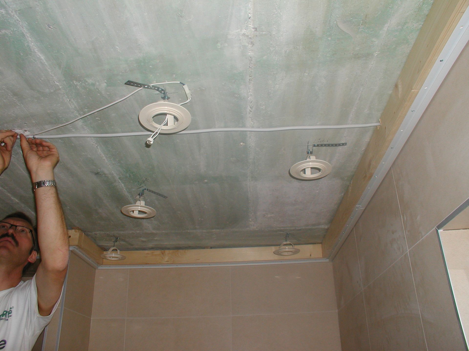 Person verkabelt Deckenleuchten in einem im Bau befindlichen Raum; grüne Trockenbauwand, Holzrahmen.