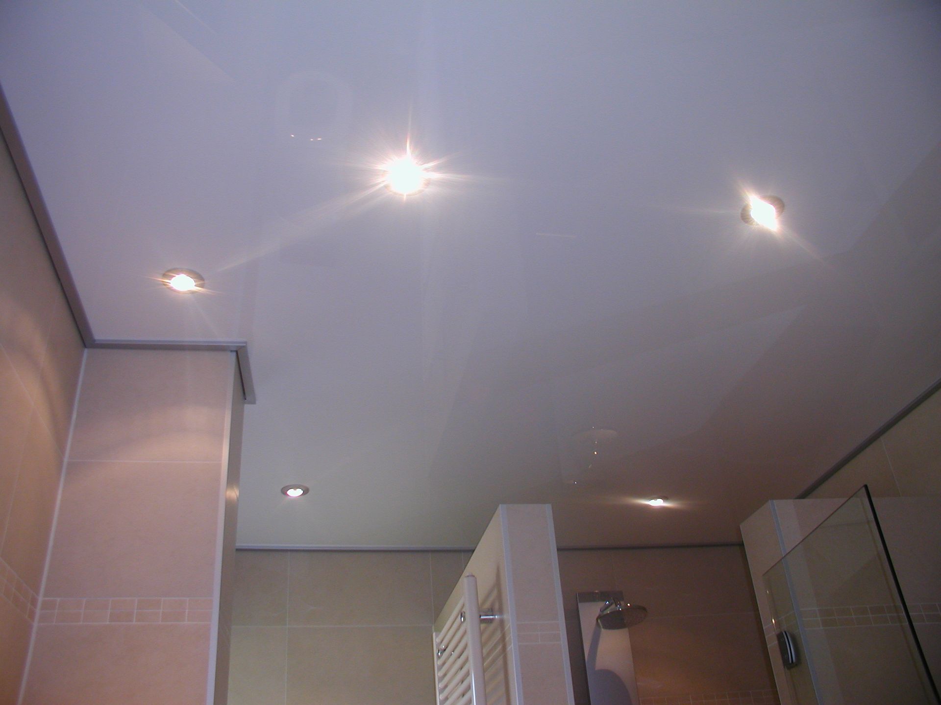 Badezimmerdecke mit Einbauleuchten, die auf der Oberfläche reflektieren.