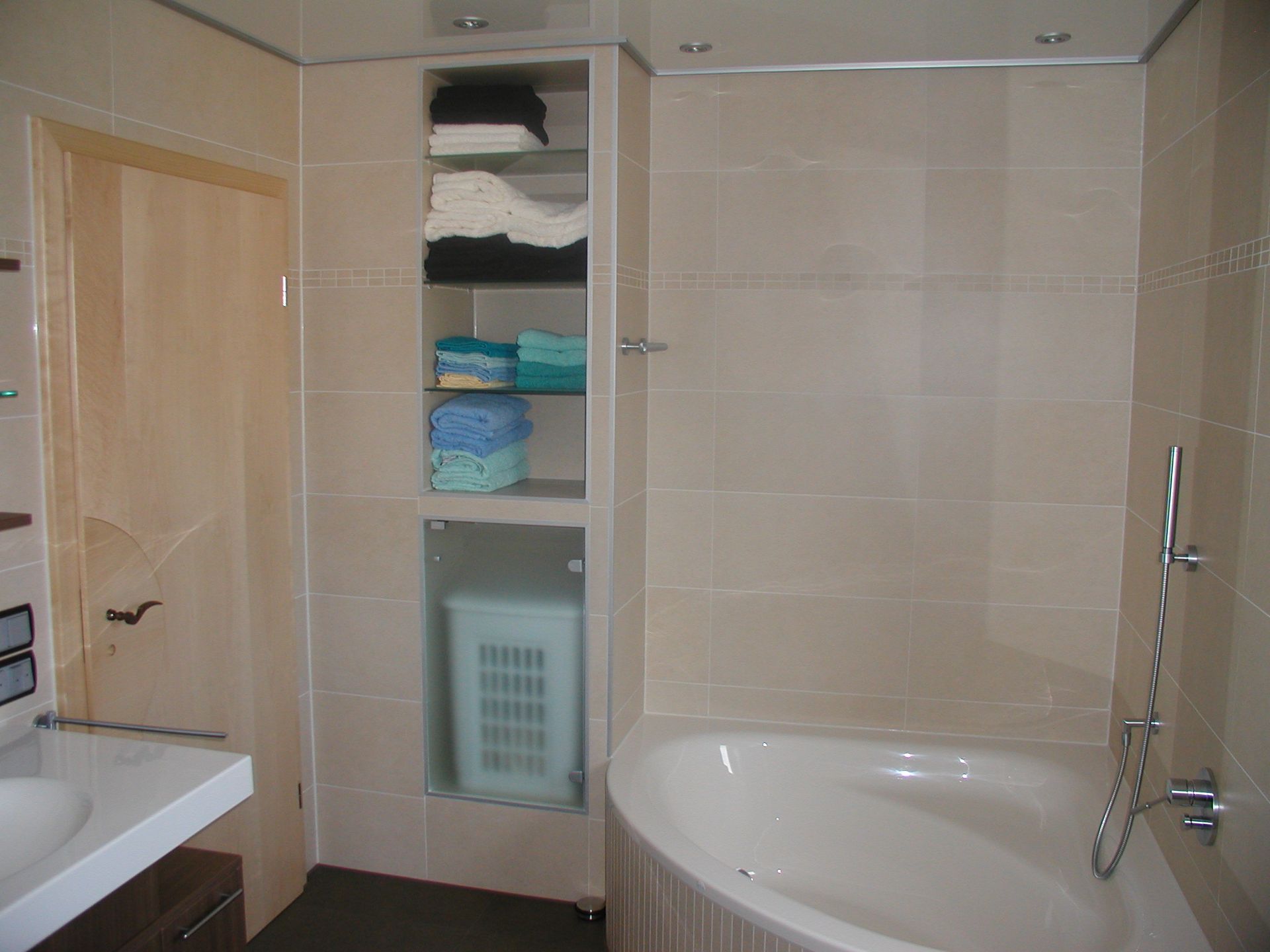 Badezimmer mit Badewanne, Regal und Tür. Beige geflieste Wände und Boden.