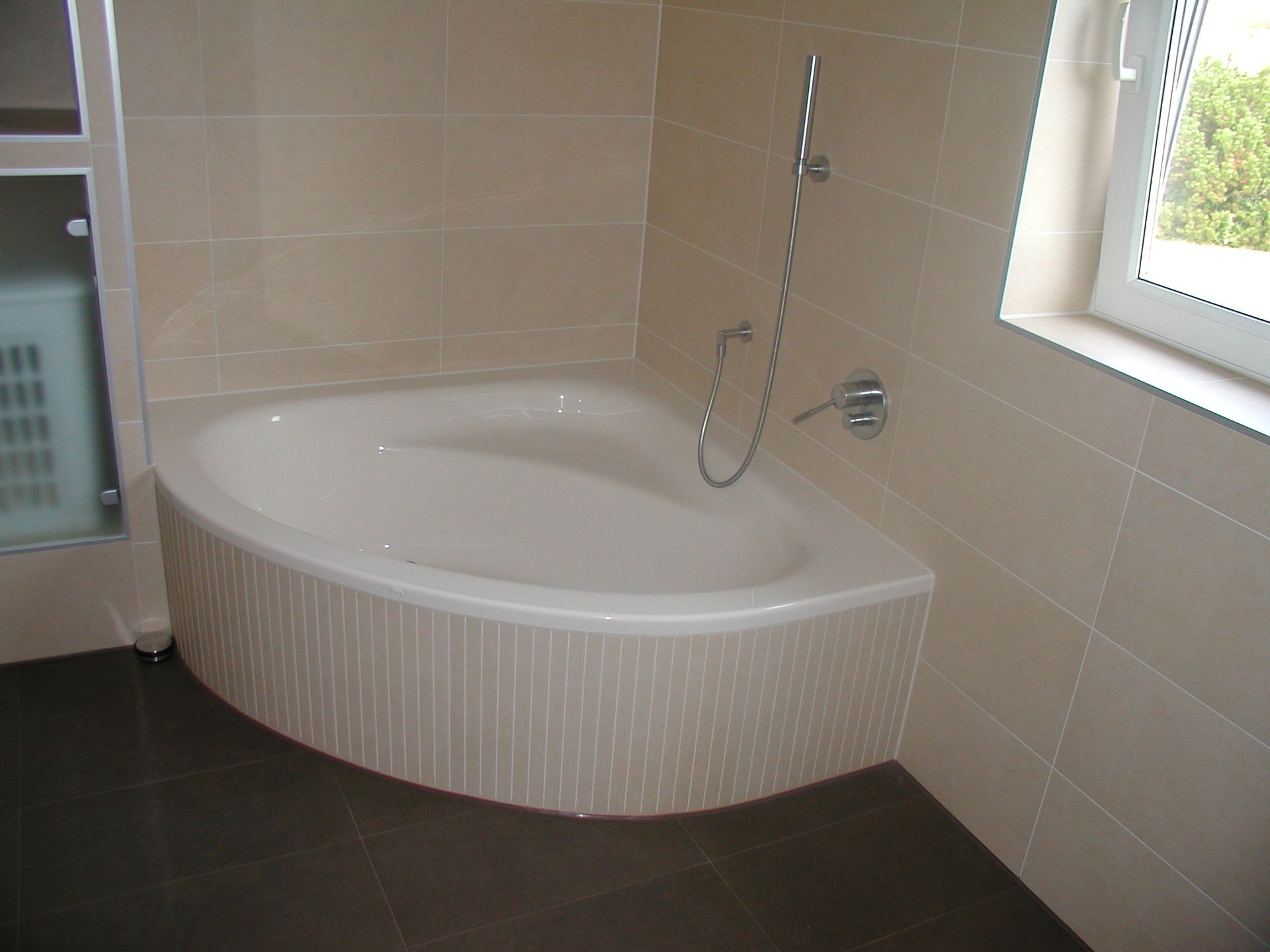 Eckbadewanne in einem Badezimmer mit beigen Fliesen und dunklem Boden.