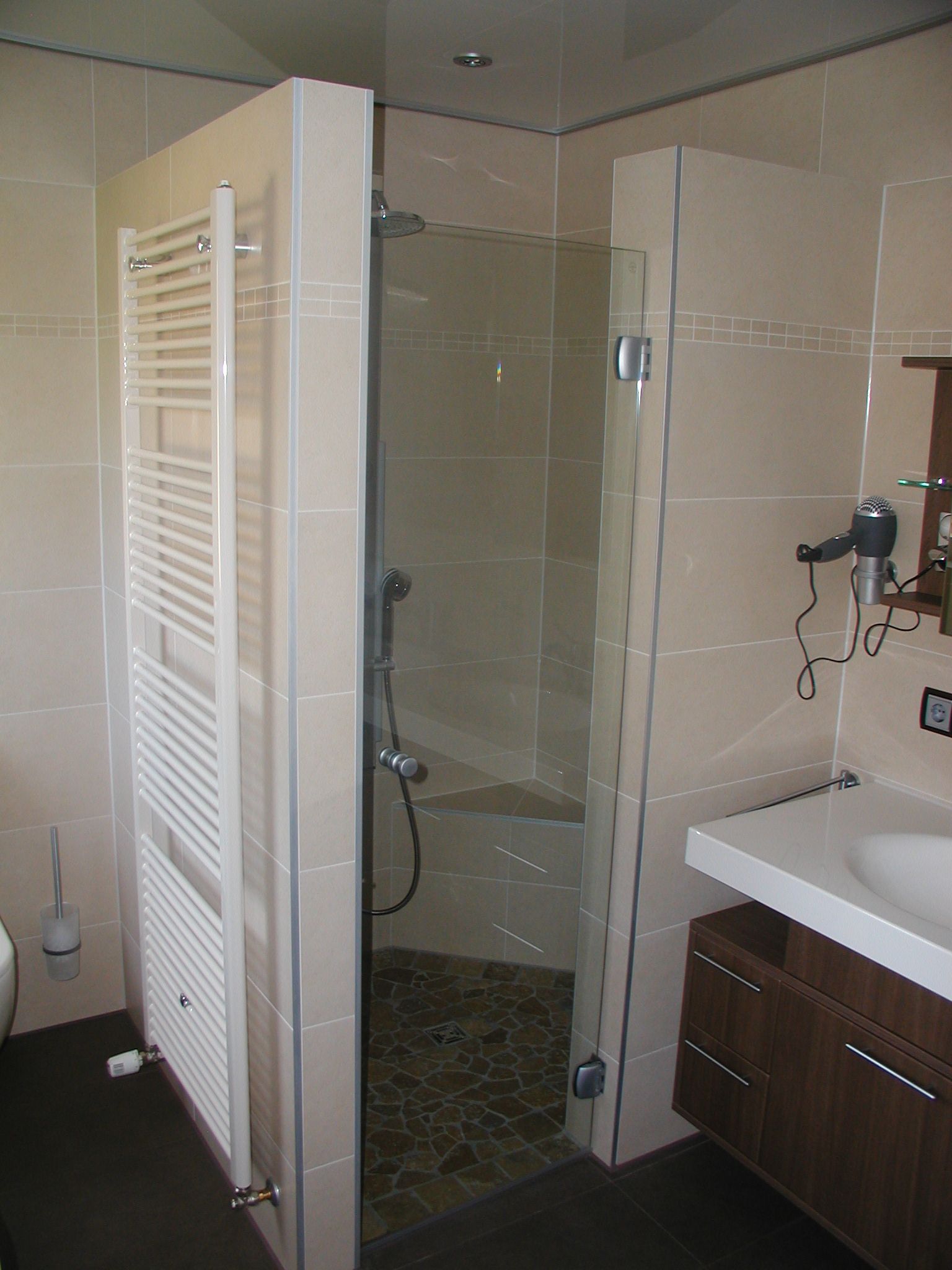 Badezimmer mit ebenerdiger Dusche, weißem Heizkörper, Waschbecken mit dunklem Holzschrank und Haartrockner.