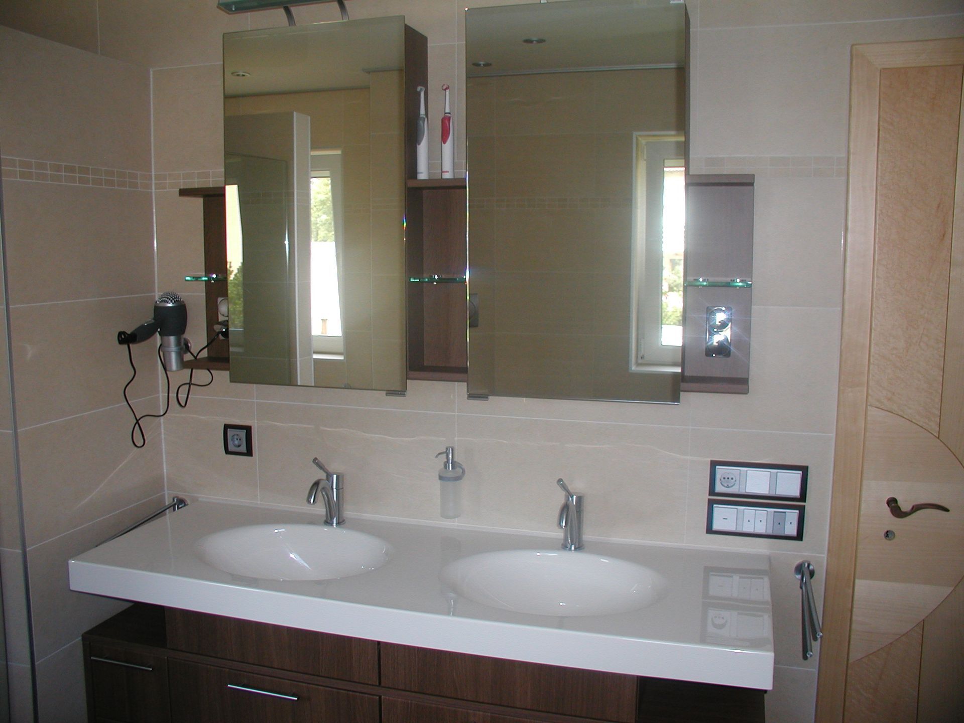 Badezimmer mit Doppelwaschtisch, zwei Spiegeln und einer hell gefliesten Wand.