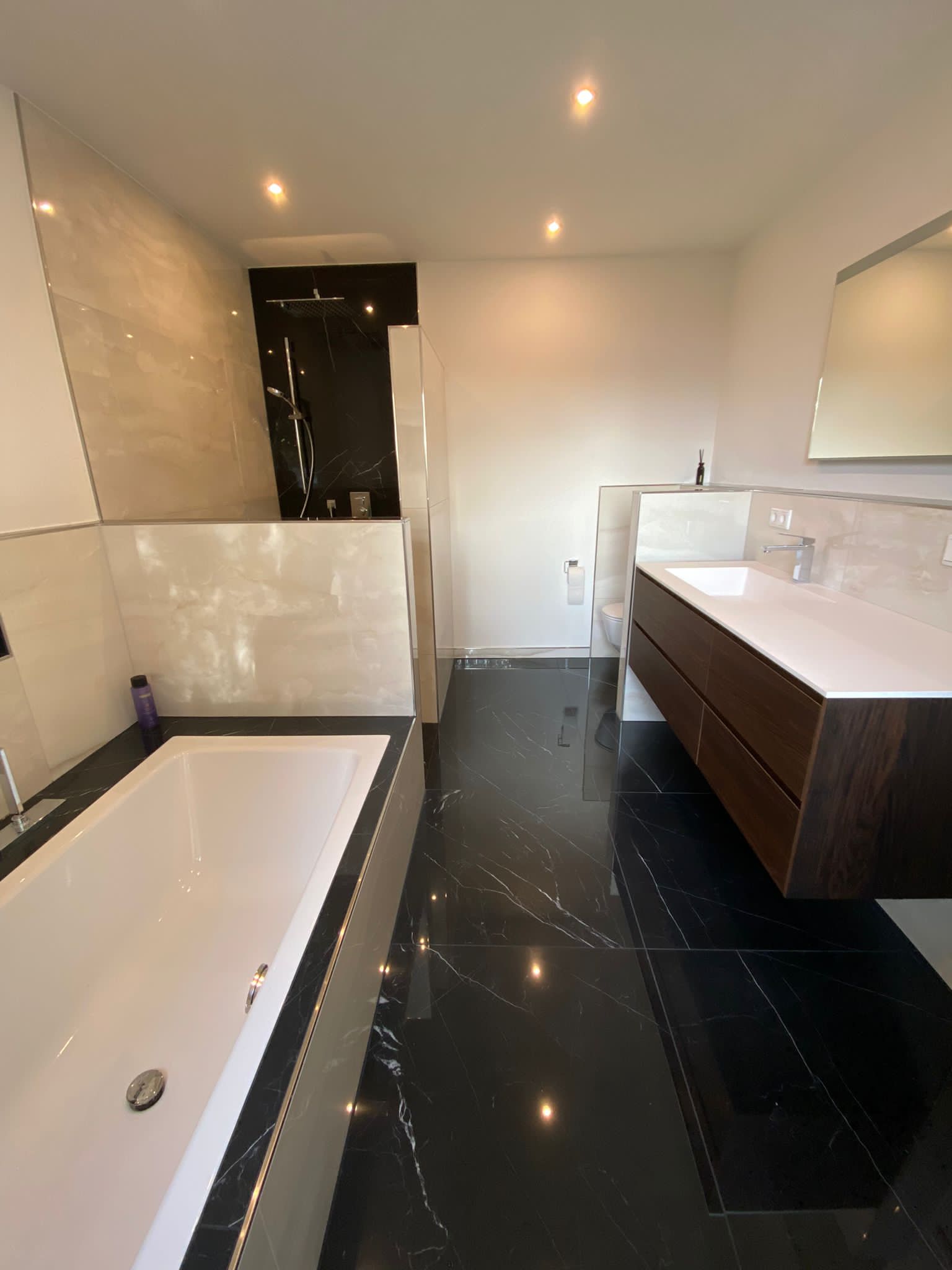 Modernes Badezimmer mit schwarzem und weißem Marmor, Waschtisch aus dunklem Holz, Badewanne.