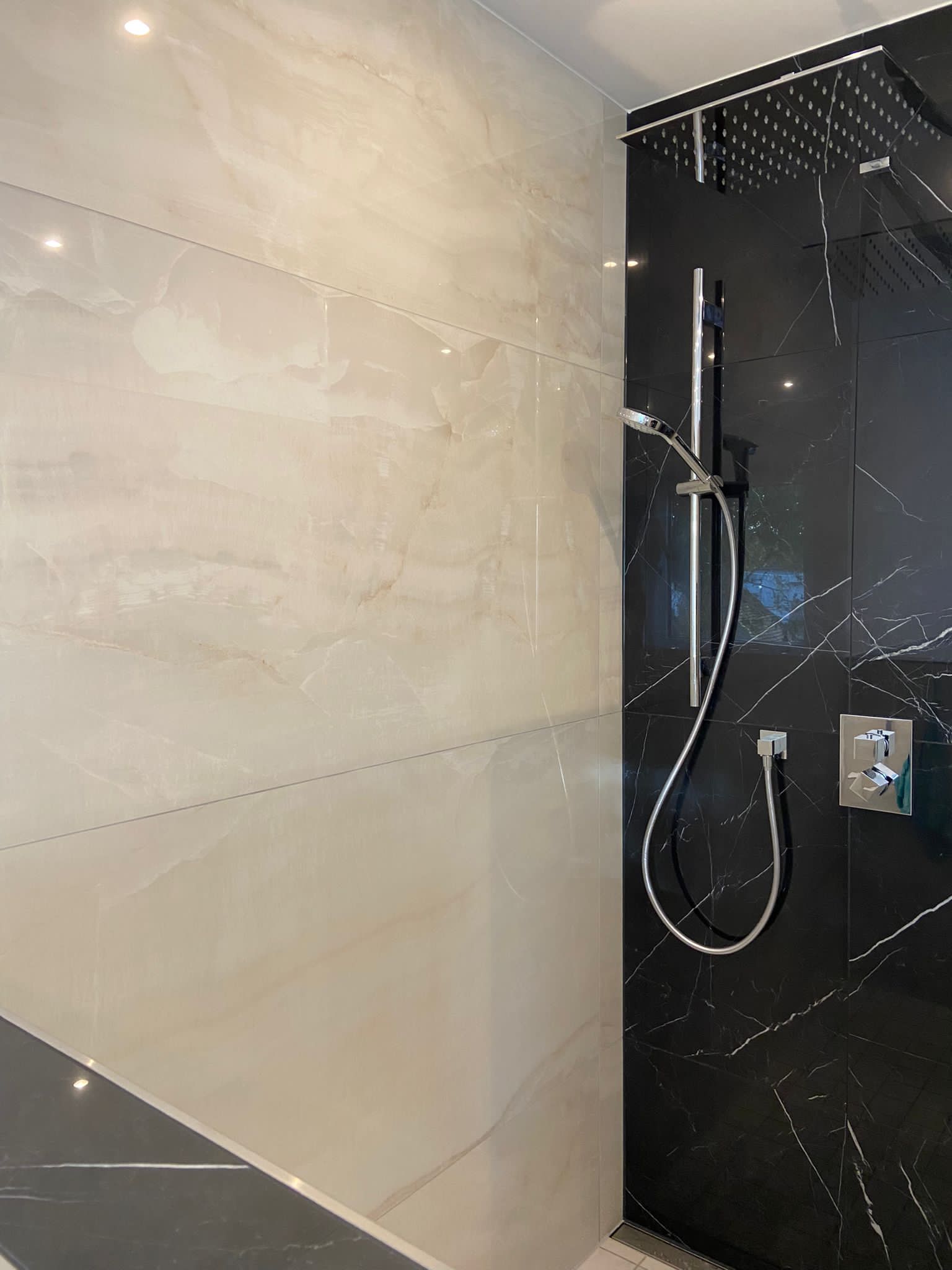Dusche mit schwarzer Marmorwand und weißen Marmorfliesen, silbernem Duschkopf und Mischbatterie.