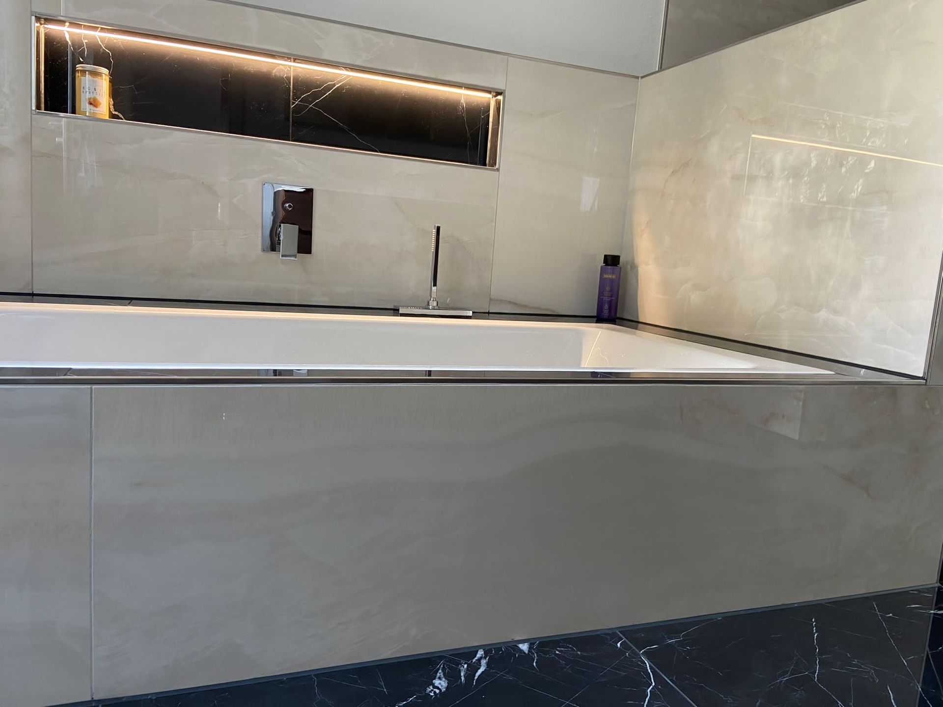 Modernes Badezimmer mit weißer Badewanne, beige gefliesten Wänden und schwarzem Marmorboden.