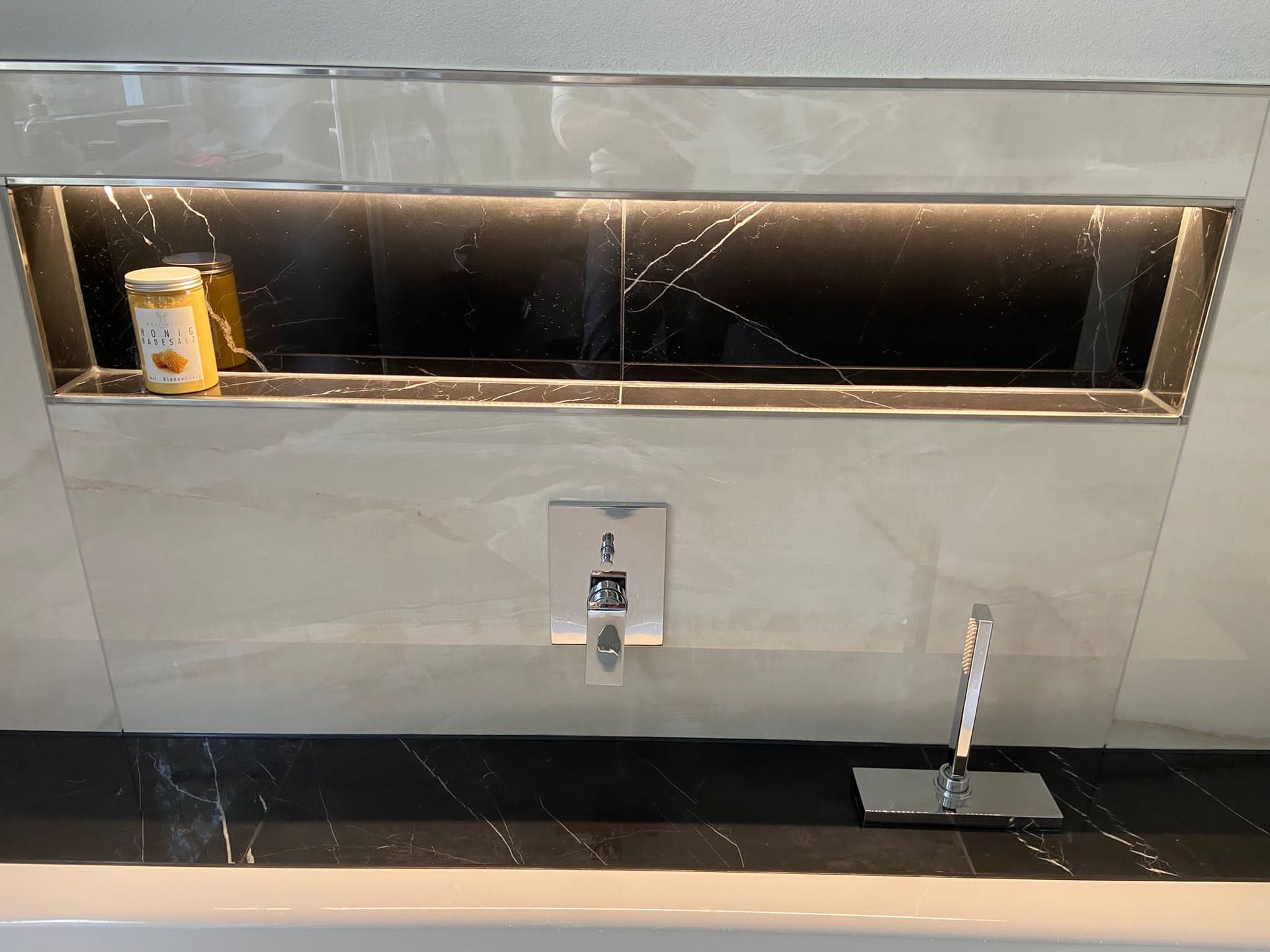 Badezimmer mit eingebautem Regal, cremefarbenen Fliesen, schwarzem Marmor und Chromarmaturen.