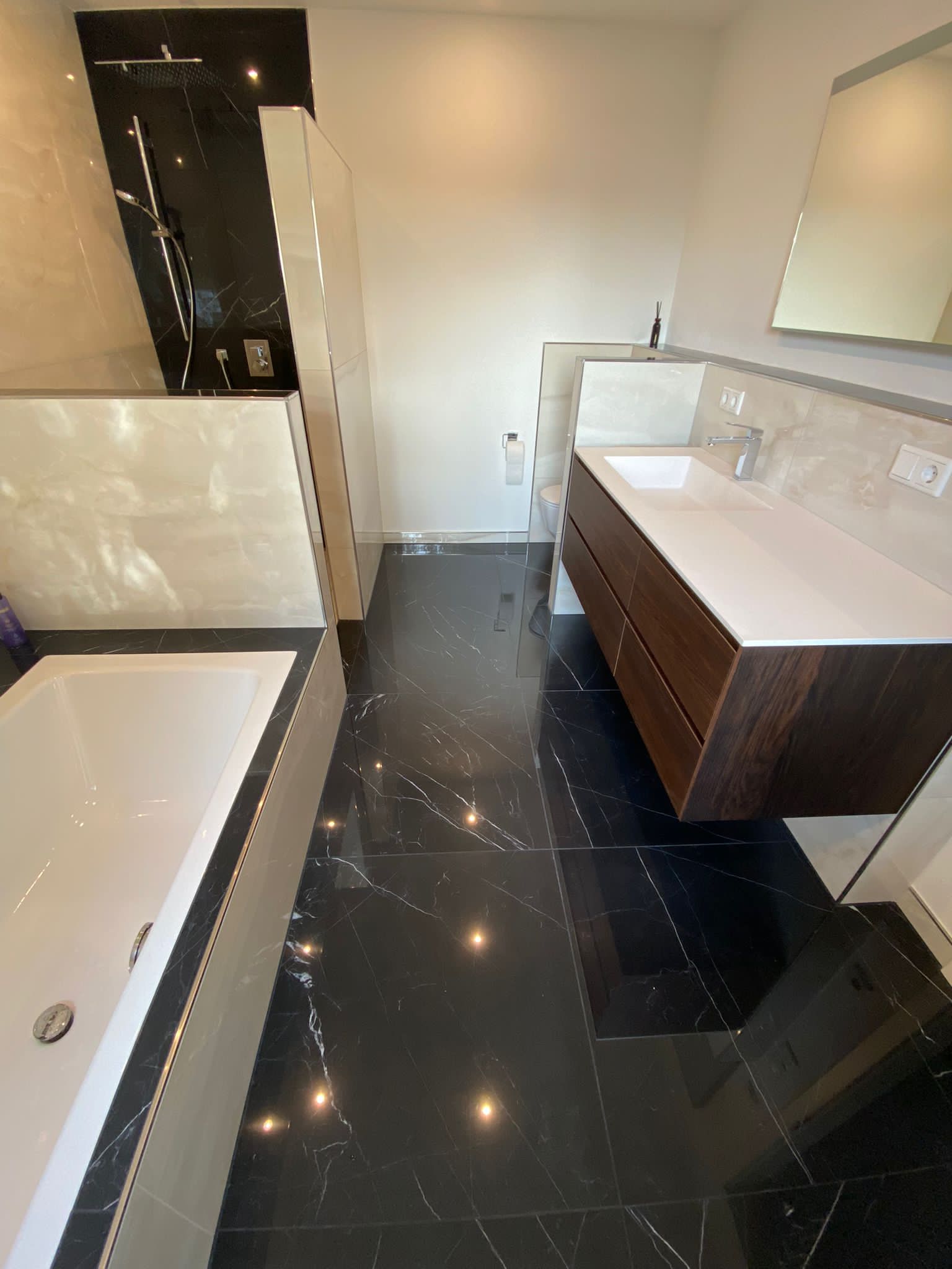 Modernes Badezimmer mit schwarzem Fliesenboden, weißer Badewanne und Waschtisch aus dunklem Holz.