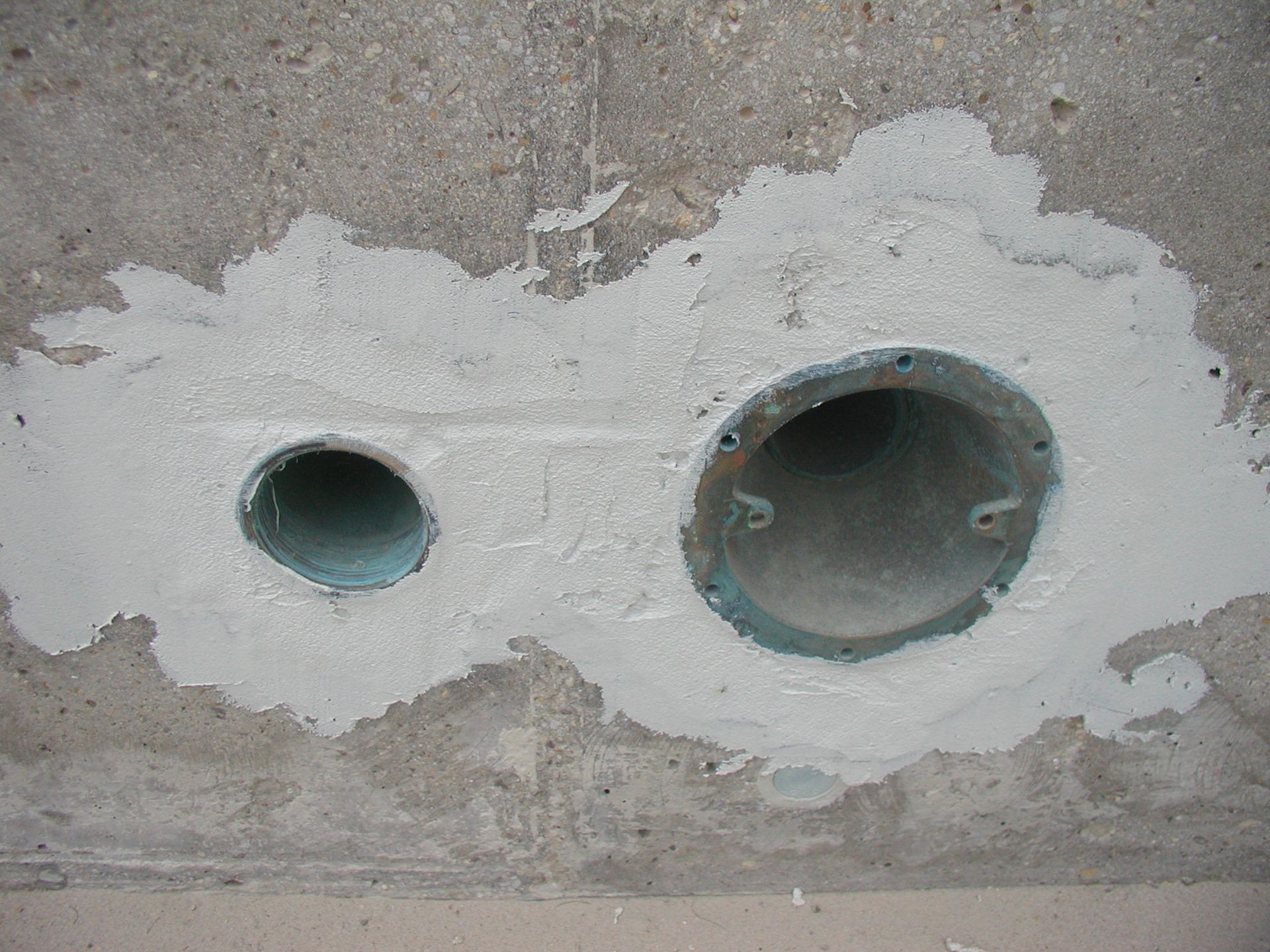Zwei kreisrunde Löcher in einer Betondecke, gefüllt mit hellem Dichtmittel.