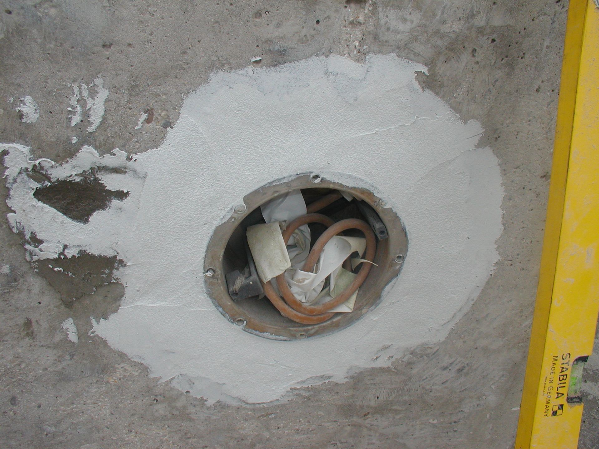 Mit grauer Masse gefülltes Loch für elektrische Leitungen in einer Betonwand.