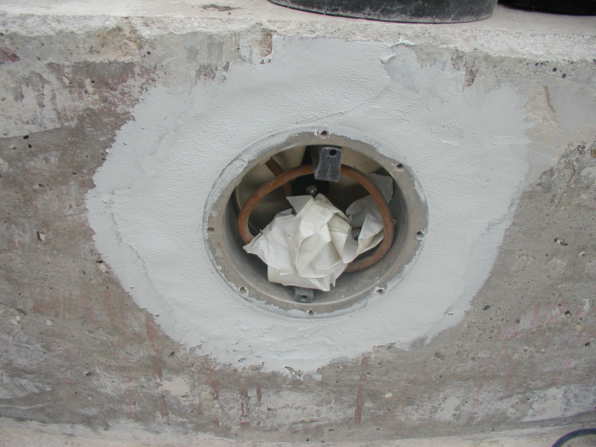 Eine Betonoberfläche mit einer runden Öffnung, die mit Papier gefüllt ist; Zement umgibt die Öffnung.
