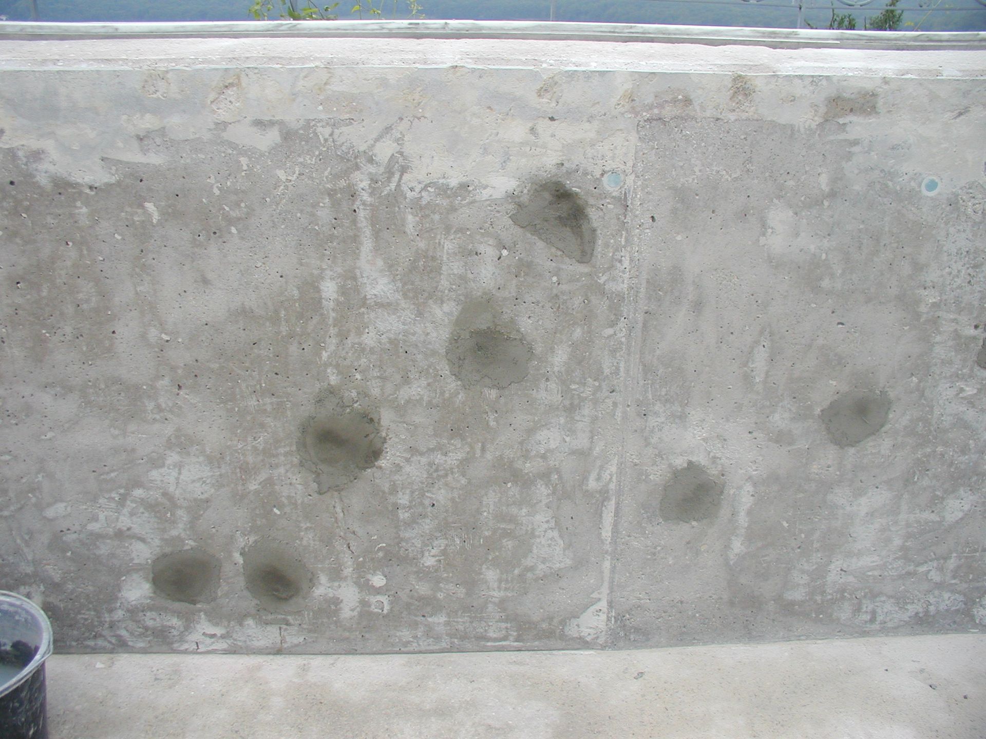 Betonwand mit mehreren geflickten kreisförmigen Löchern.