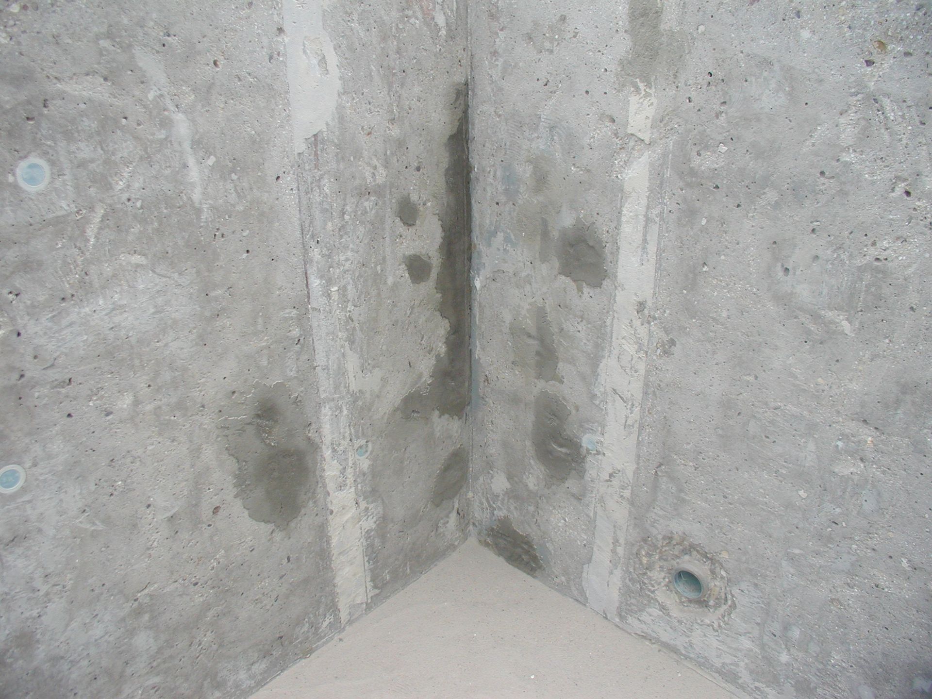 Betonecke mit feuchten Stellen und einem Abflussloch.
