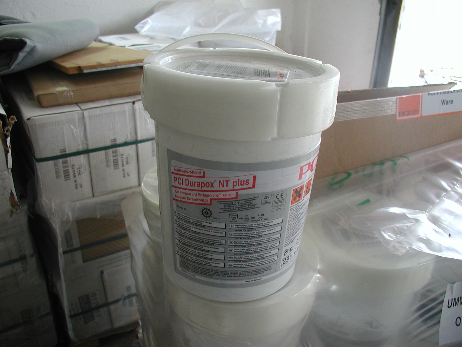 Weiße Plastikwanne mit der Aufschrift „D-Super Fine“, mit anderen gestapelt, in einer unordentlichen Lagerumgebung.