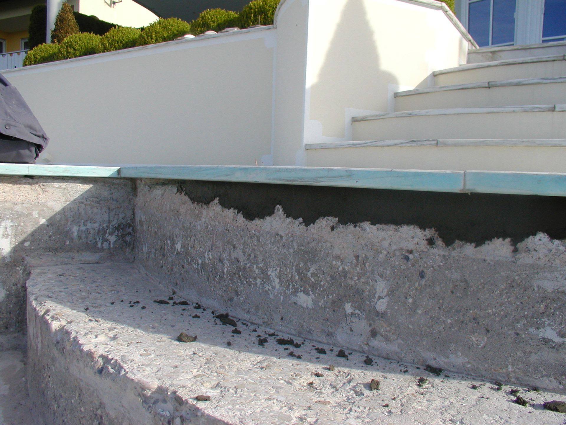 Betonstufen und Beckenrand im Bau, im Hintergrund eine weiße Wand und Treppen.