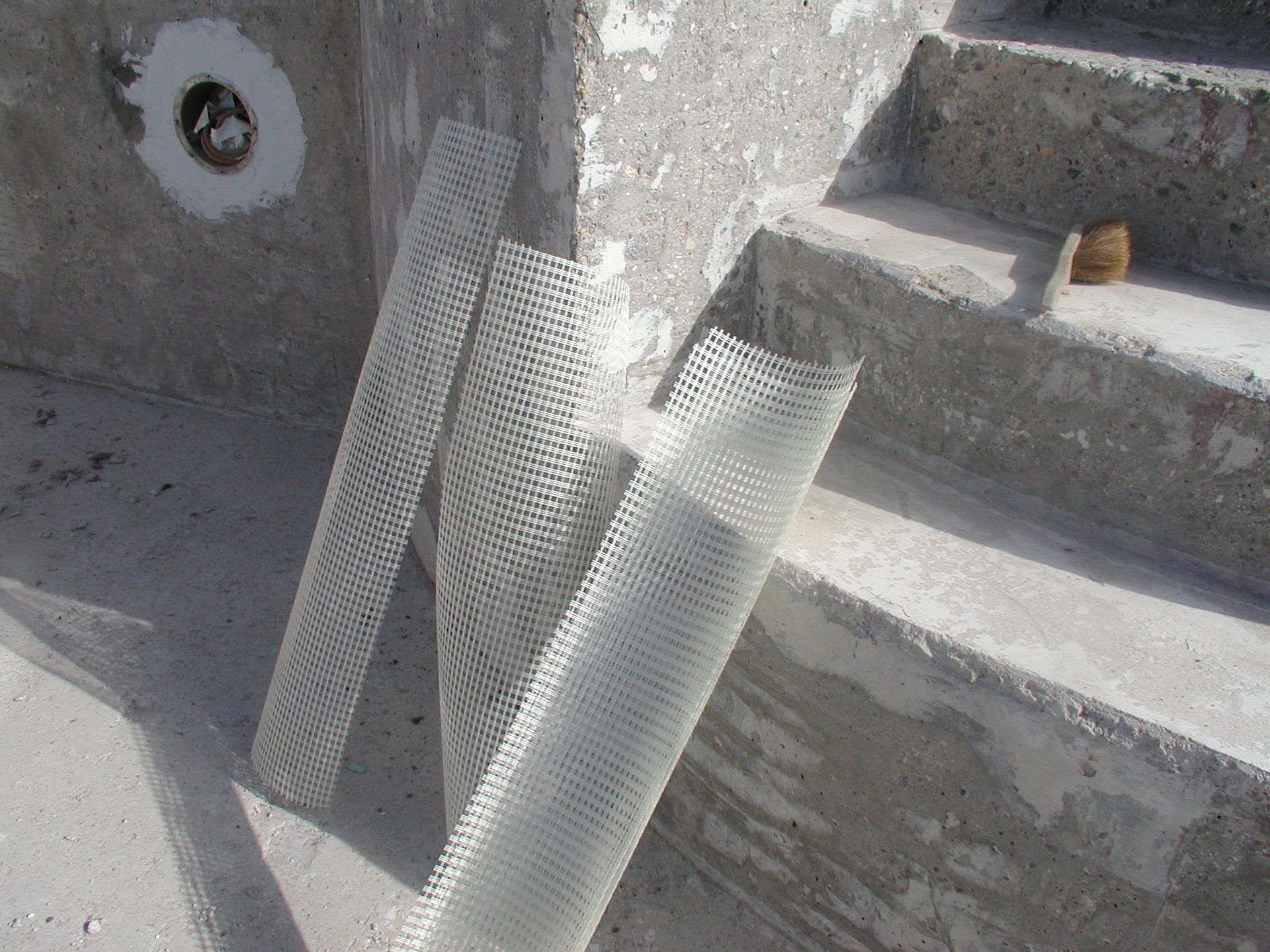 Drei Rollen weißes Kunststoffnetz, die an einem Betonbecken mit Treppe anliegen.