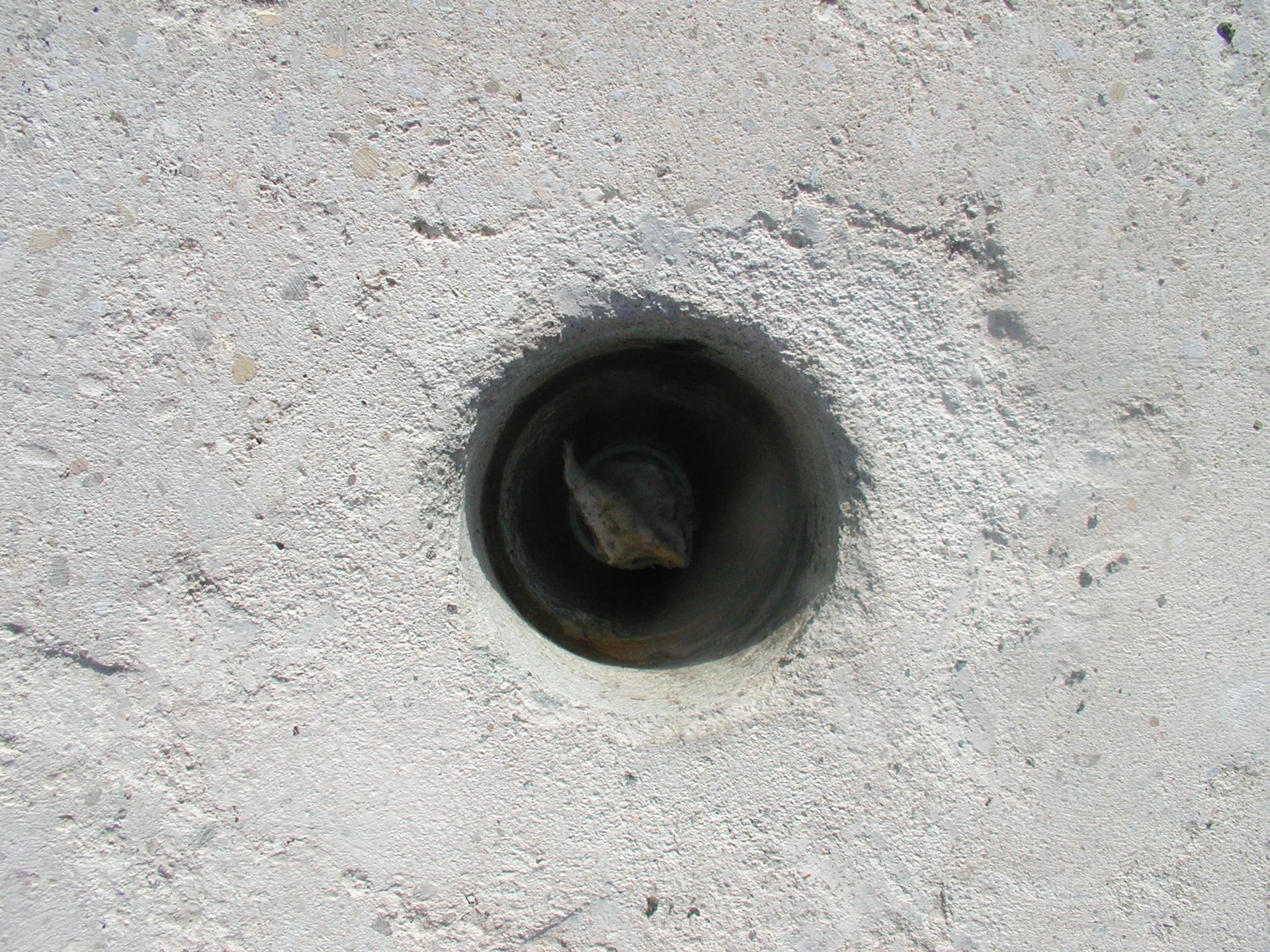 In Beton gebohrtes Loch, im Inneren ist ein dunkler Metallstab sichtbar.
