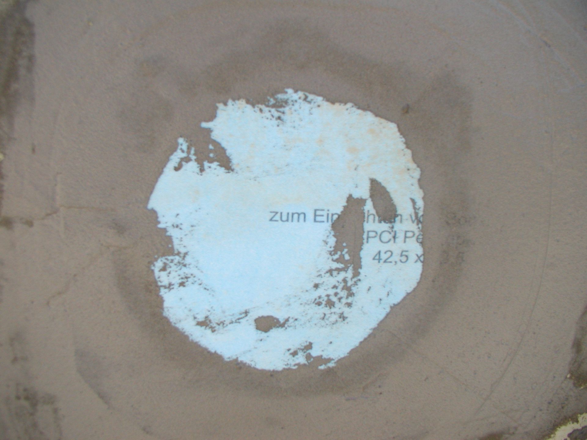 Weißes, beschädigtes Etikett auf braunem Untergrund, mit teilweise sichtbarem Text: „Zum Einh…PCI Pa…42,5 x“