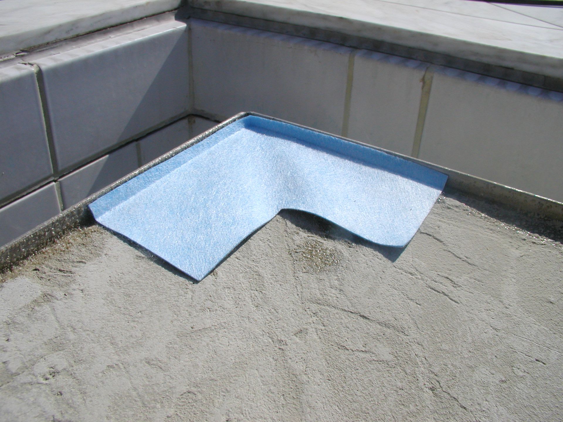 Blaues Eckstück aus Schaumstoff auf einer Betonoberfläche, in der Nähe einer gefliesten Wand, das einen rechten Winkel bildet.