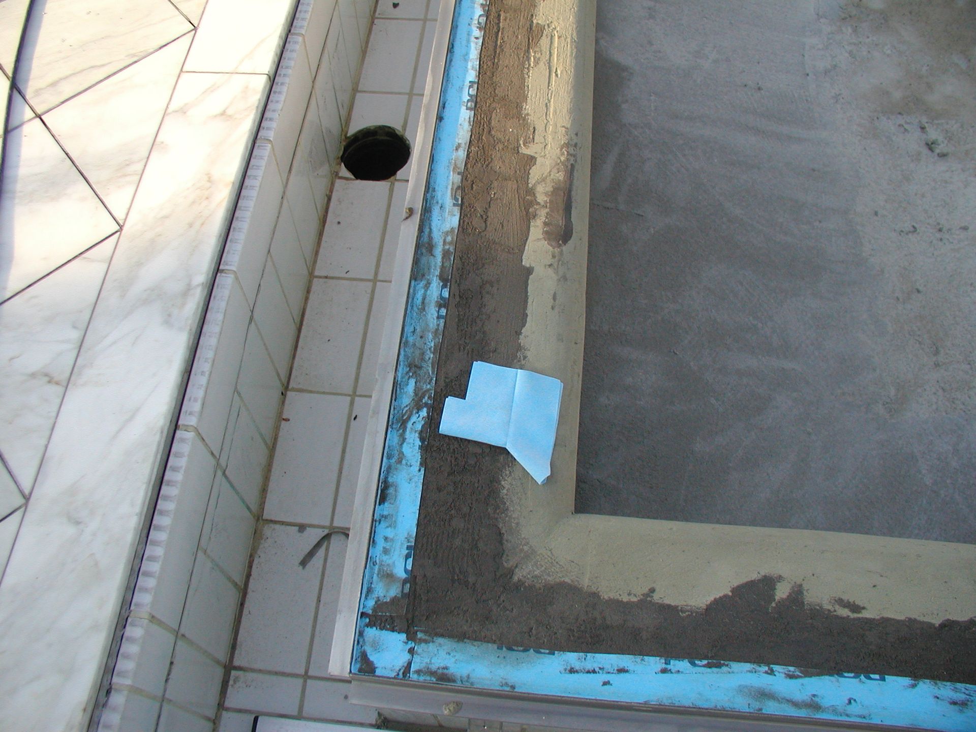 Poolkonstruktion: Betonbeckenrand mit blauem Dichtungsband, Ablauf und angrenzender Marmorfliesen.