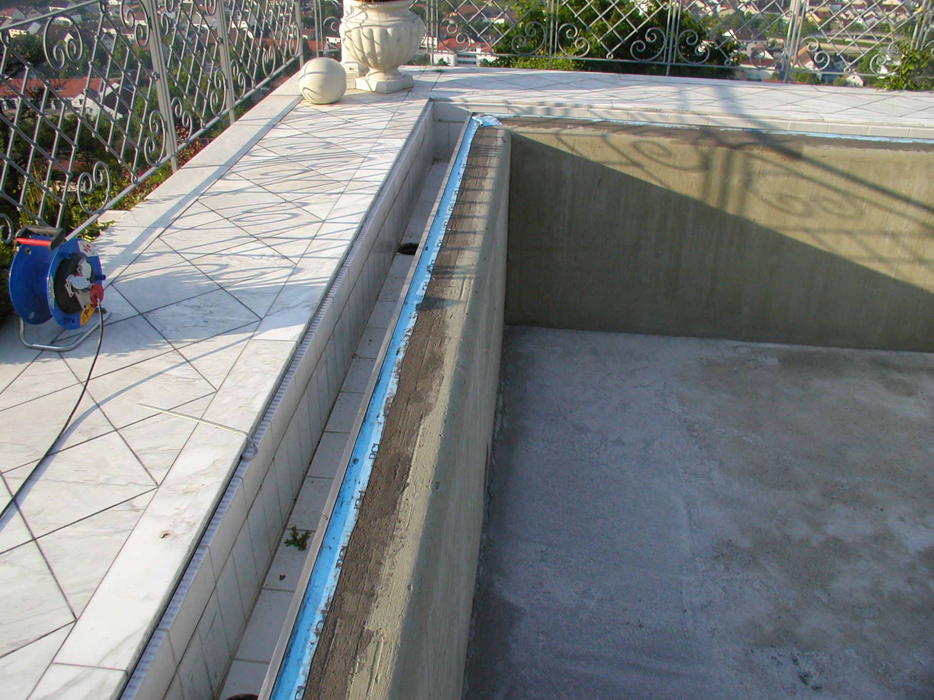 Dach mit Poolrand, umgeben von einer Mauer. Blaue Schaumstoffverkleidung und ein Metallgeländer an der Seite.