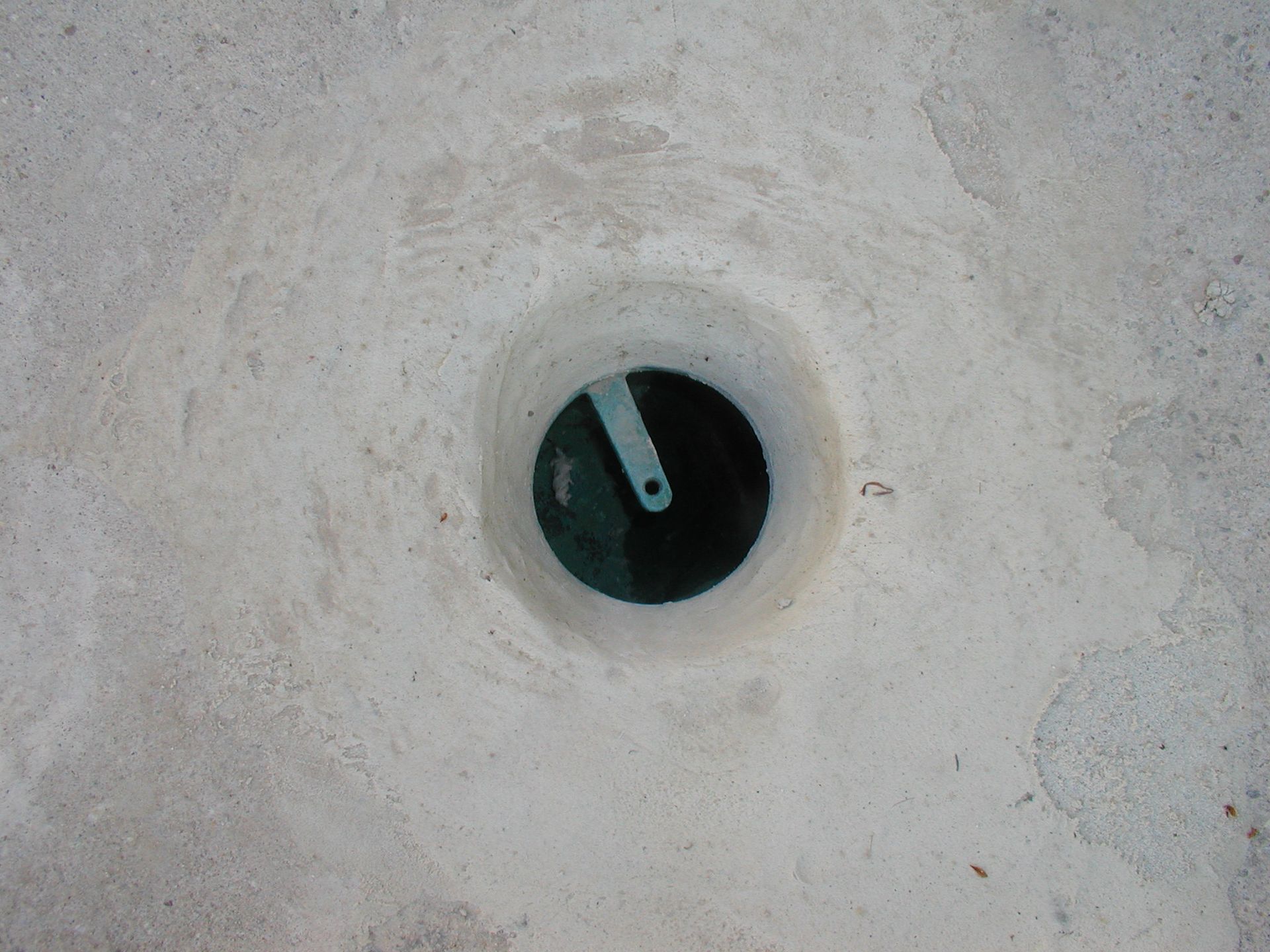 Ein kleiner runder Wasserablauf mit einem in Beton eingelassenen Metallgriff.