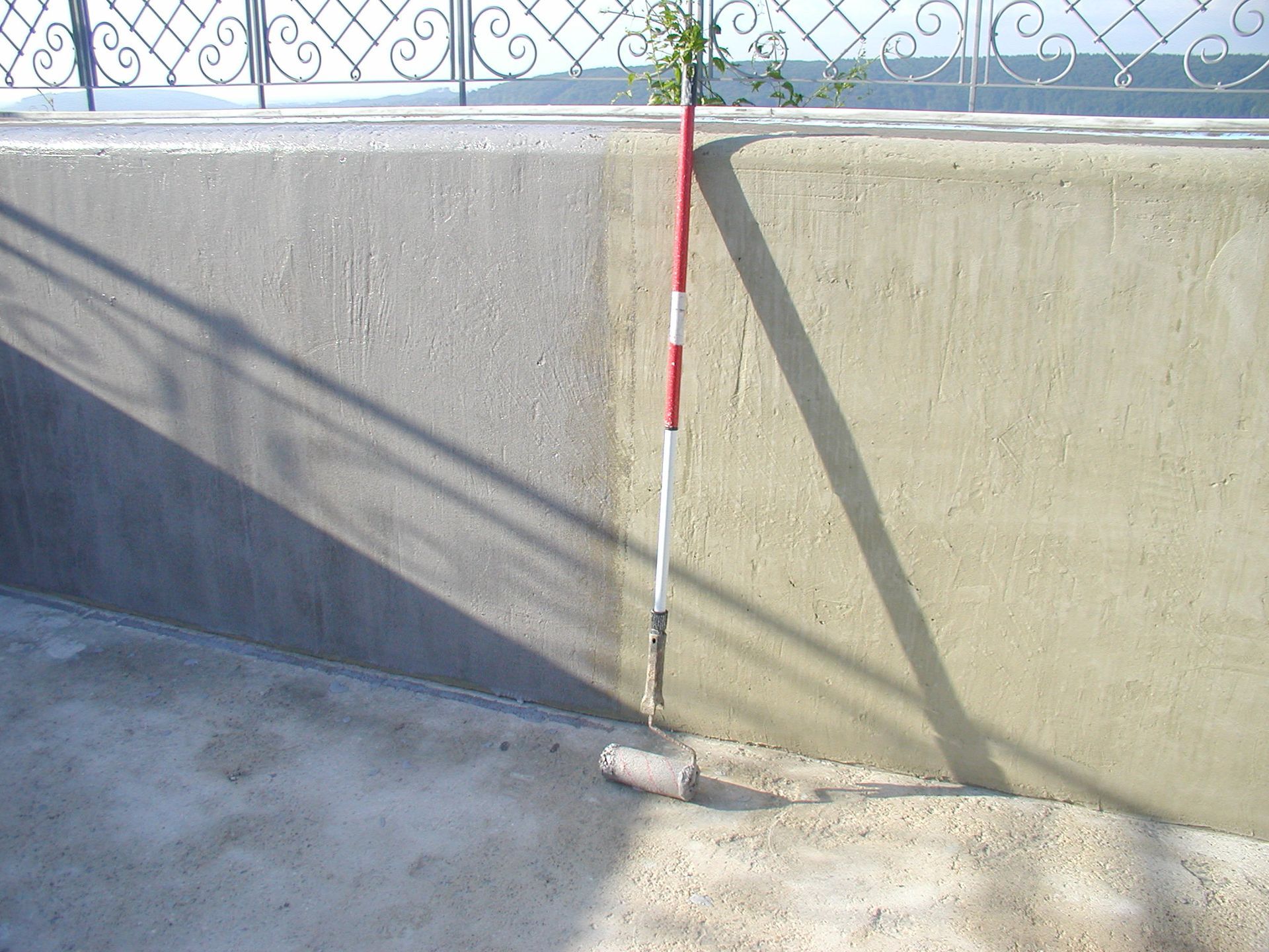 Betonwand mit einem rot-weiß gestreiften Stock, schrägem Schatten und einem kleinen Betonblock.