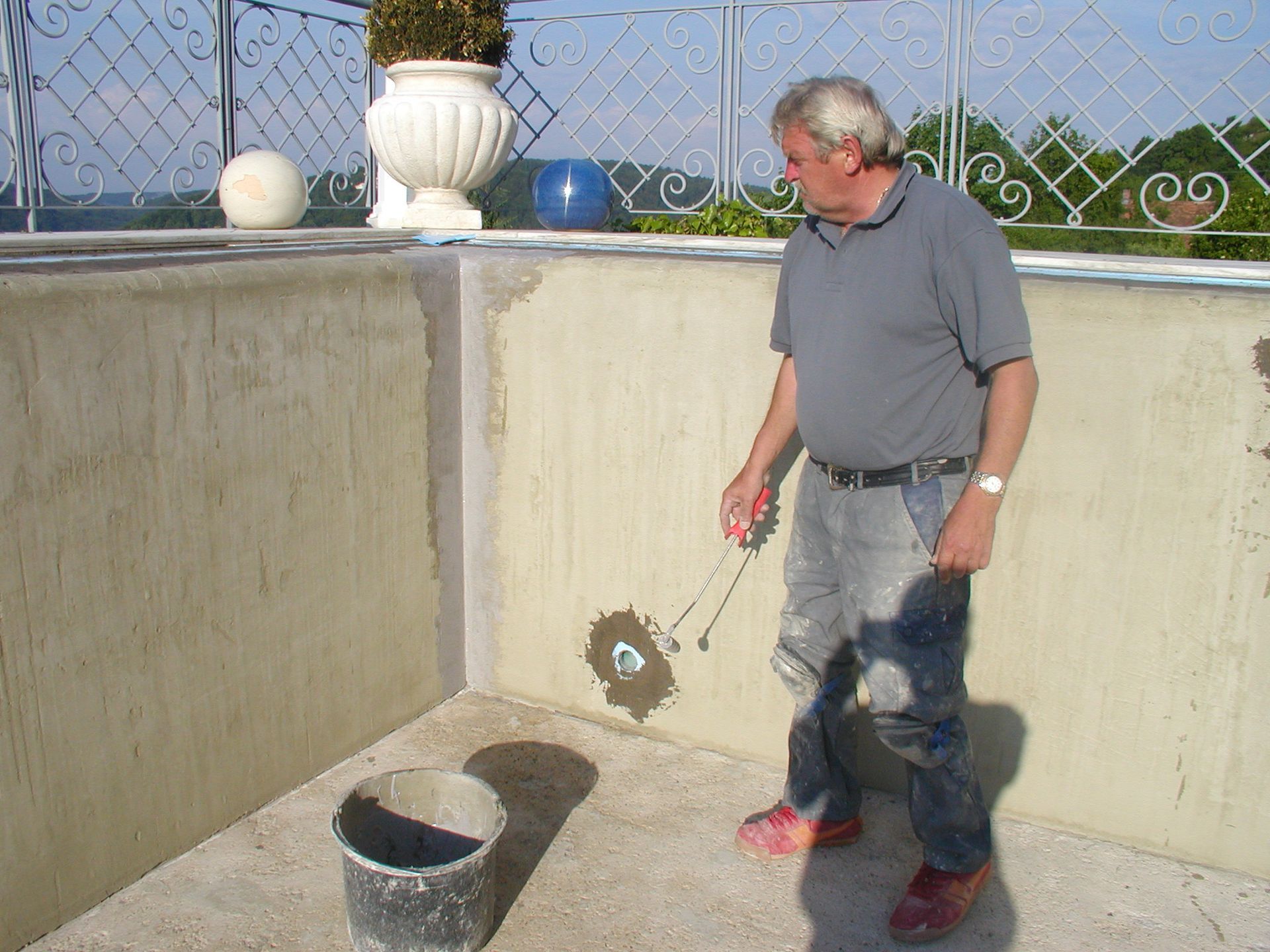 Mann flickt eine Wand, hält Werkzeuge, Eimer auf dem Boden, Außenaufnahme.