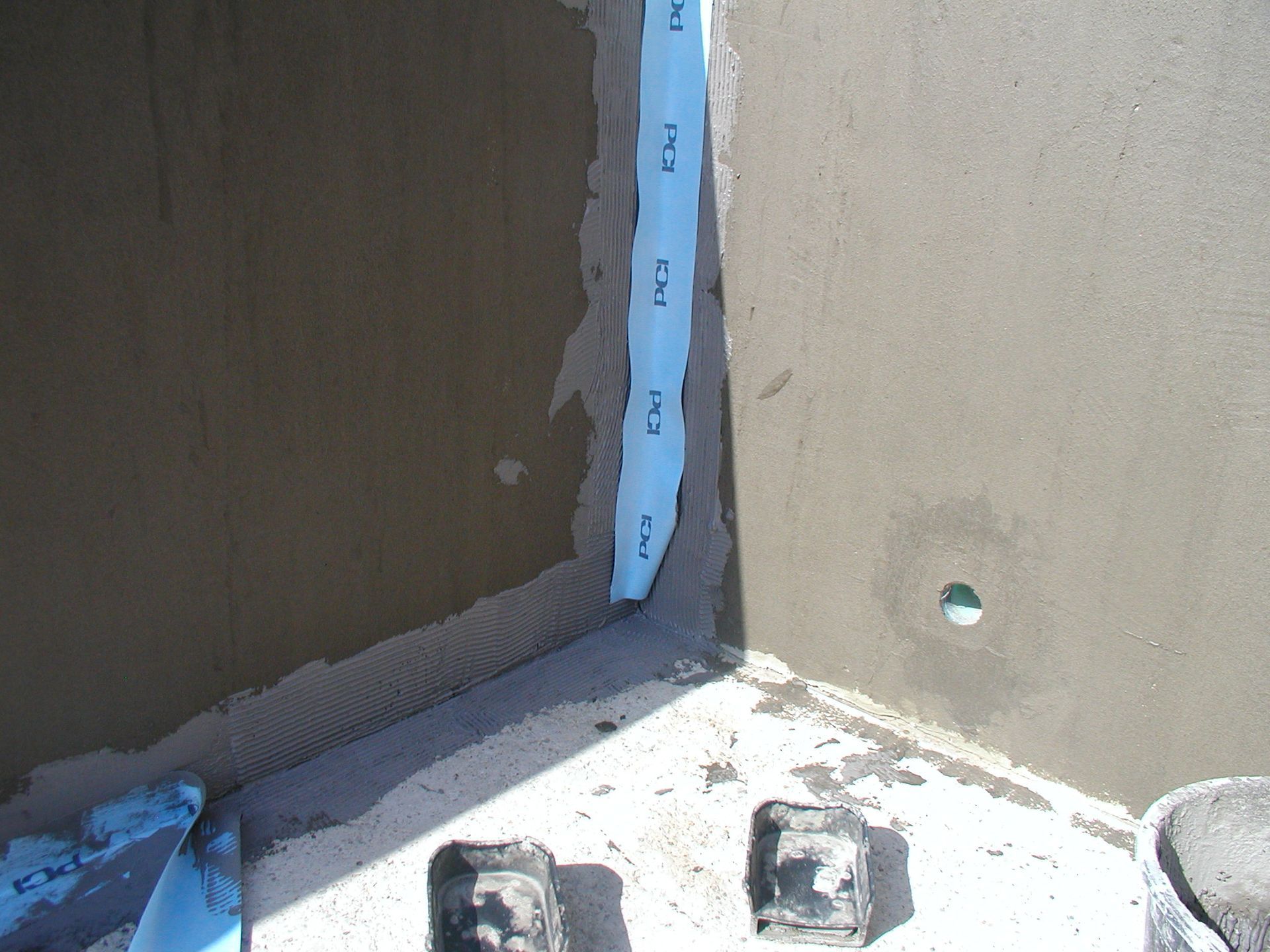 Ecke eines im Bau befindlichen Gebäudes mit blauem Abdichtungsband zwischen Beton und Stuck.