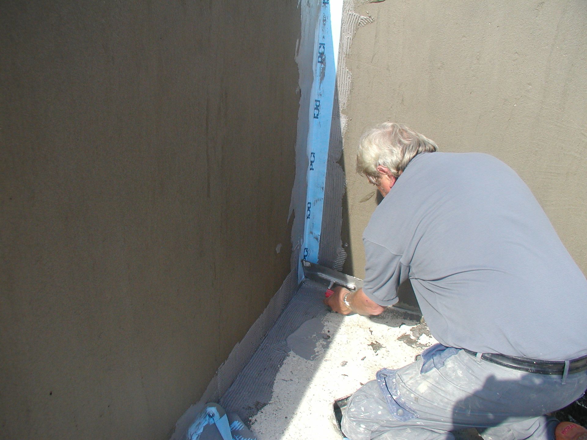 Mann trägt im Freien mit einer Kelle und blauem Klebeband Dichtungsmittel auf eine Ecke auf.