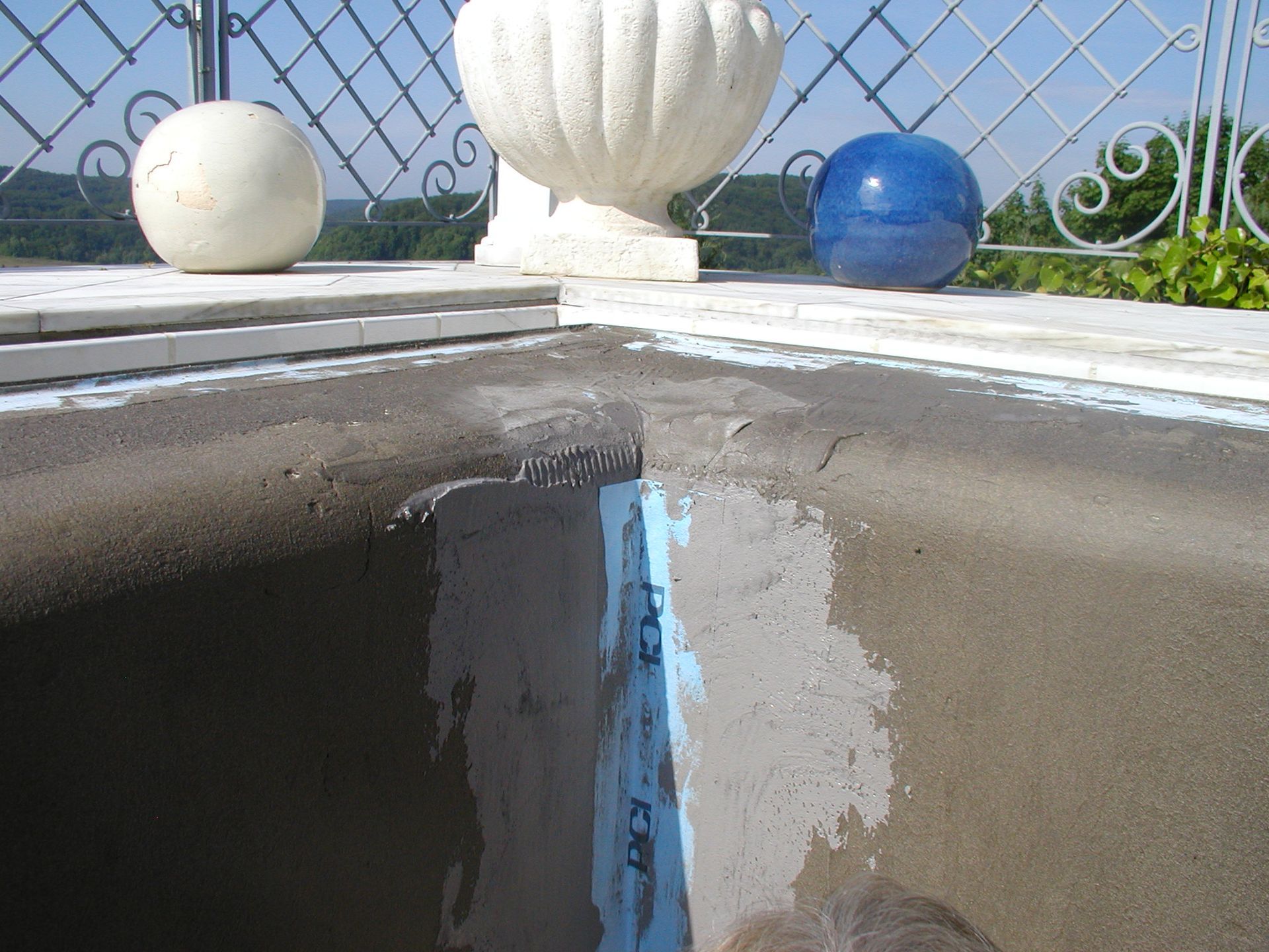 Nahaufnahme einer Betonoberfläche mit blauem Klebeband und Feuchtigkeit, möglicherweise zur Abdichtung einer Balkonecke, mit dekorativen Kugeln und einer weißen Vase.