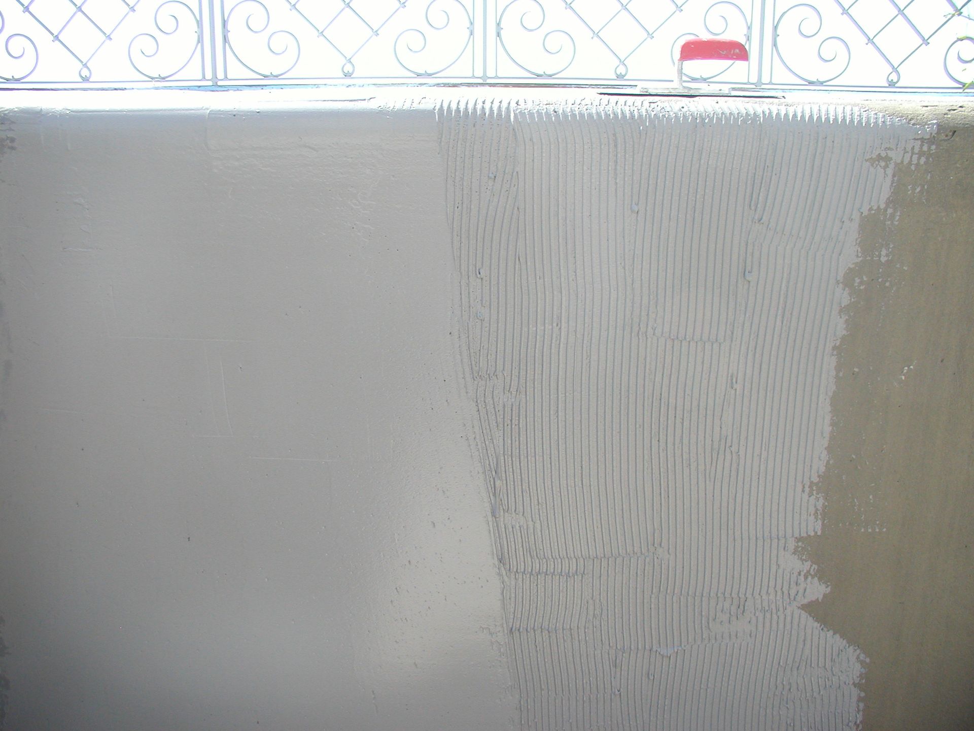 Eine graue, frisch verputzte Wand mit einem vertikalen, strukturierten Muster auf der rechten Seite.