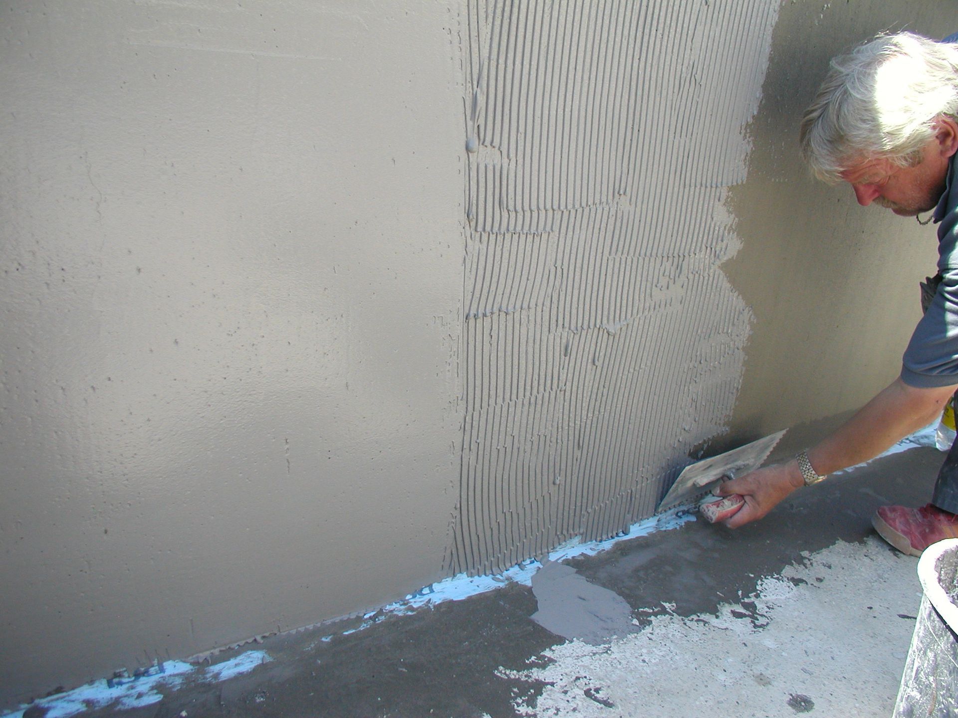 Mann trägt mit einer Kelle Mörtel zum Fliesenlegen auf eine Wand auf.