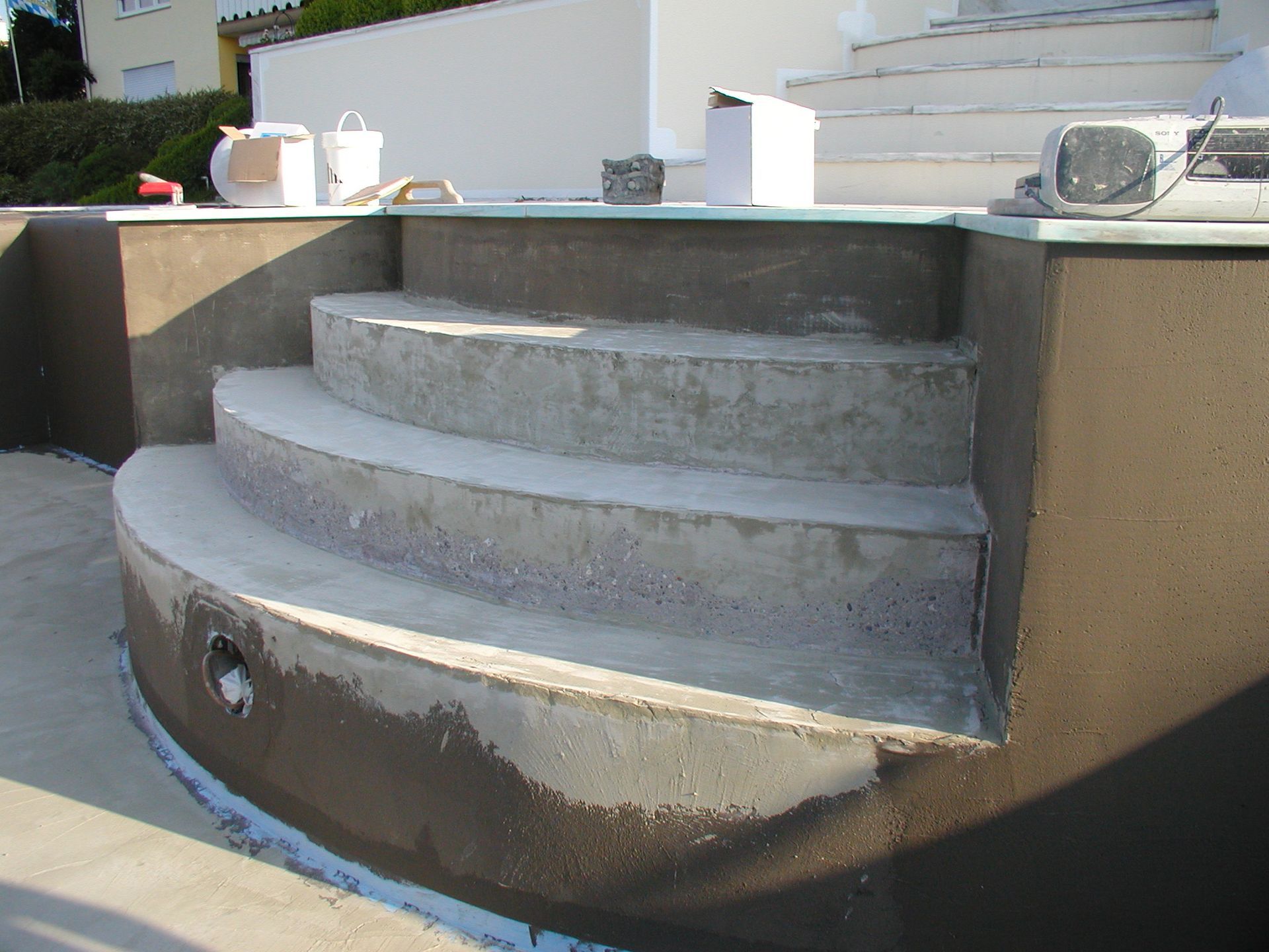 Betonstufen mit brauner Kante, eingebaut in einen Pool. Bauwerkzeuge und Materialien sind vorhanden.