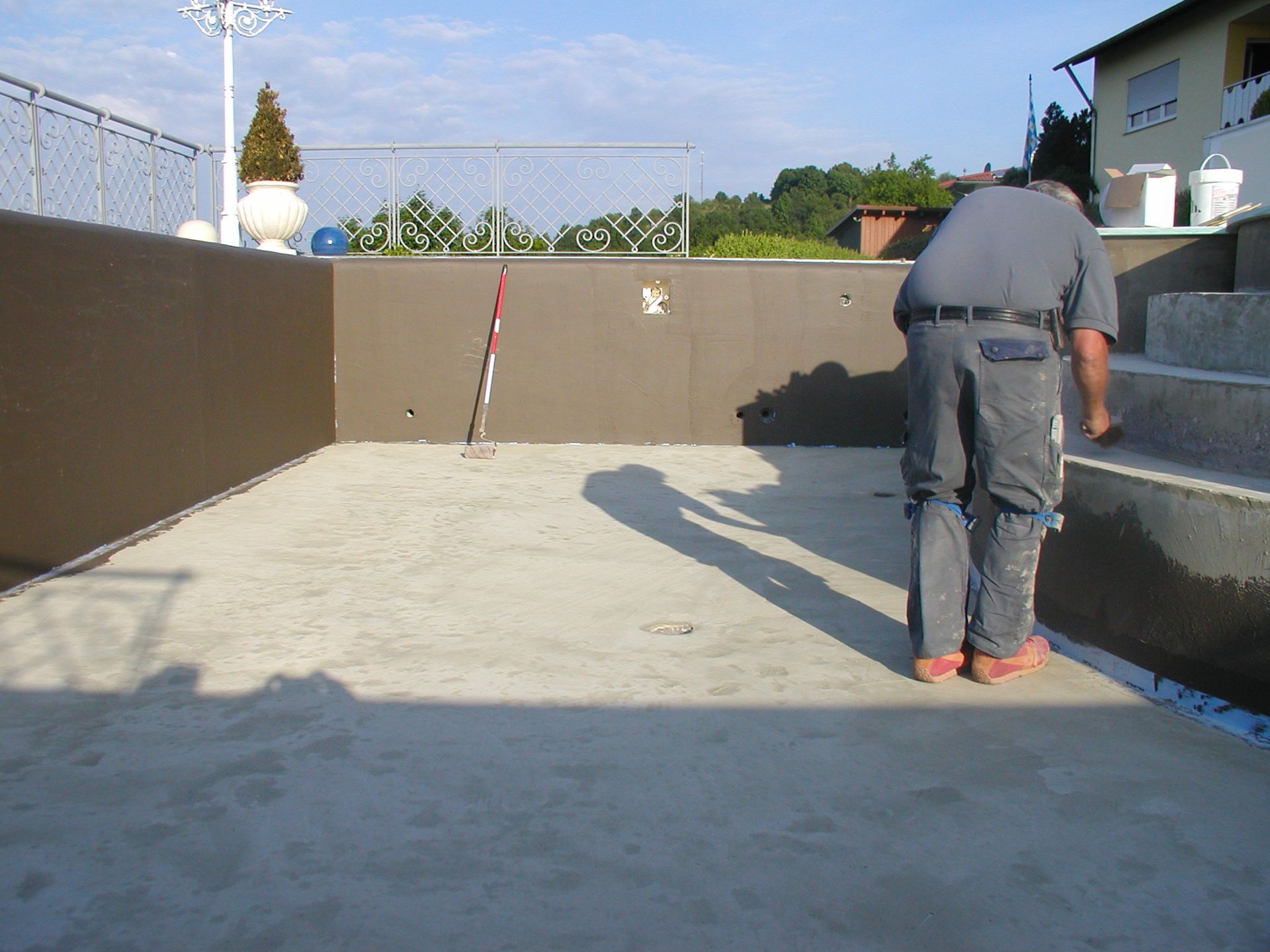 Mann streicht einen Betonpool, braune Wände, Stufen, helles Tageslicht, im Freien.