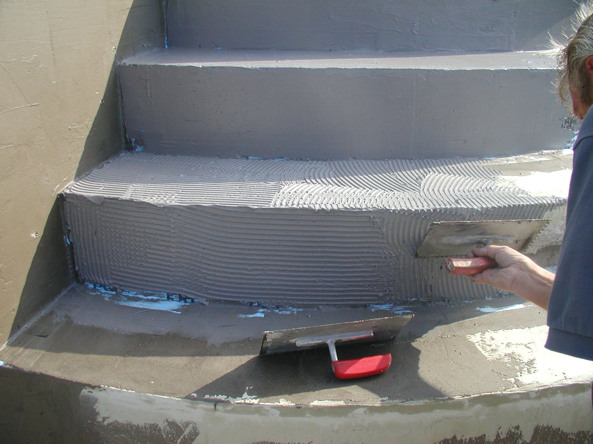 Person, die mit einer Kelle grauen Mörtel auf Betonstufen im Außenbereich aufträgt.