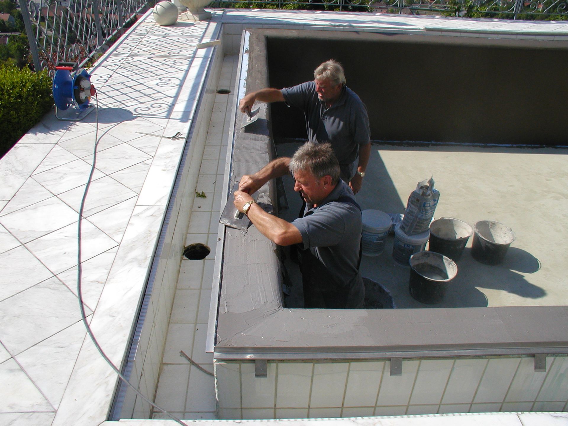 Zwei Männer arbeiten am Rand eines Pools und tragen Dichtungsmittel auf. Beton mit Marmorrand.