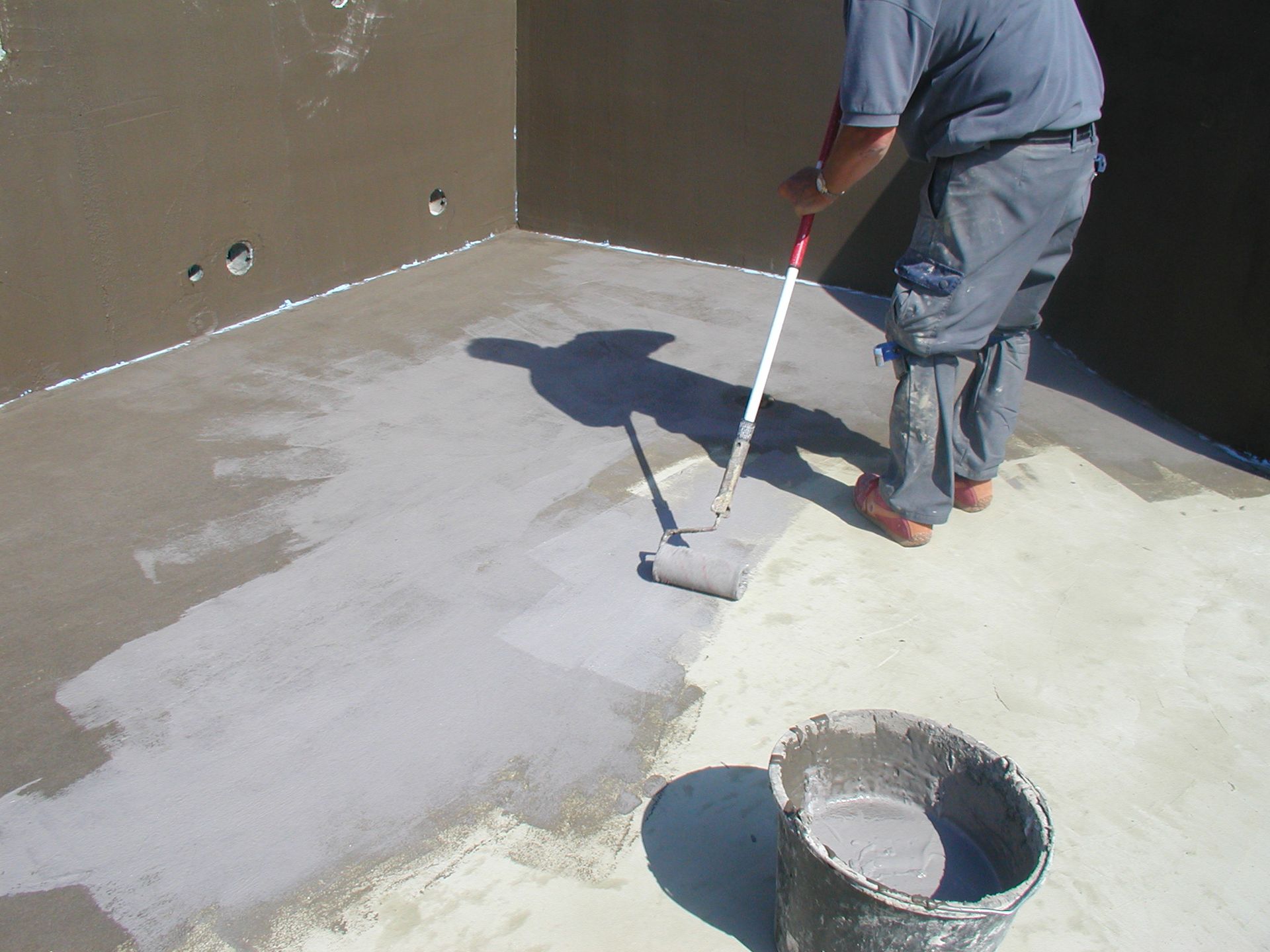Eine Person trägt eine graue Versiegelung auf einen Betonboden und Betonwände auf.
