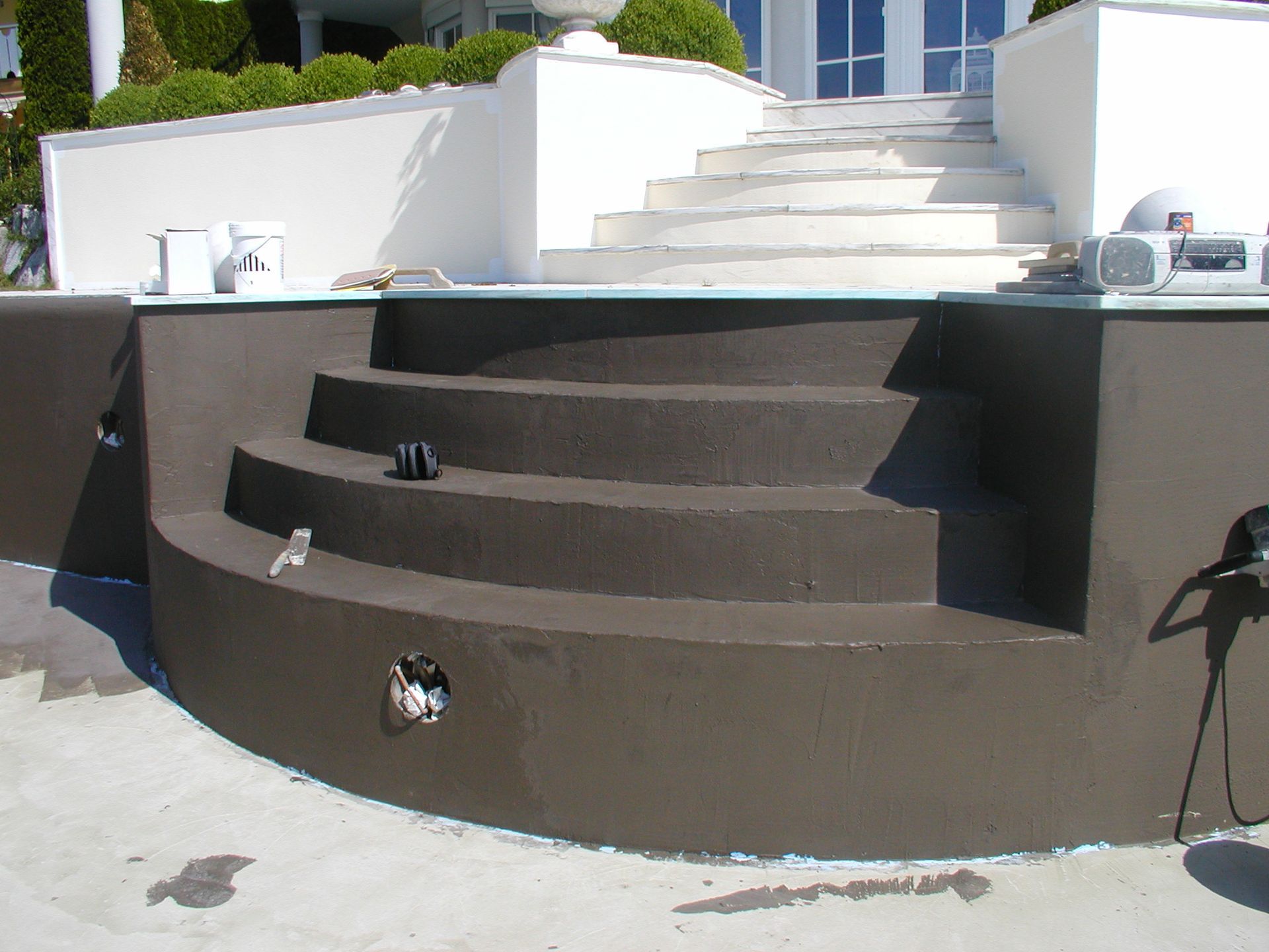 Ein braun gestrichener Pool mit geschwungenen Stufen, weißen Treppen und einem Gebäude im Hintergrund.