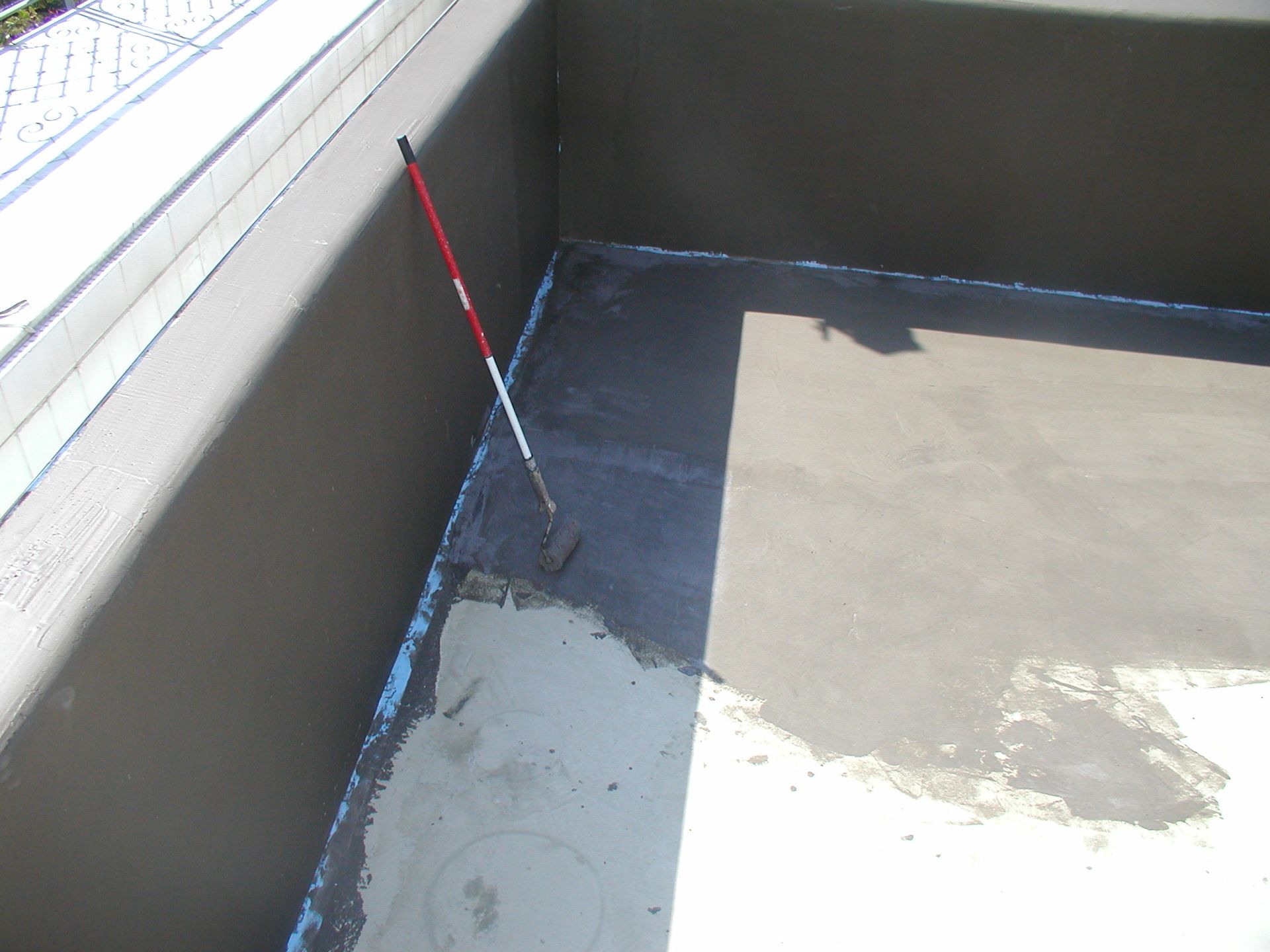 Auftragen einer dunkelgrauen Versiegelung auf den Rand eines Flachdachs mit einer Rolle an einem langen Griff.