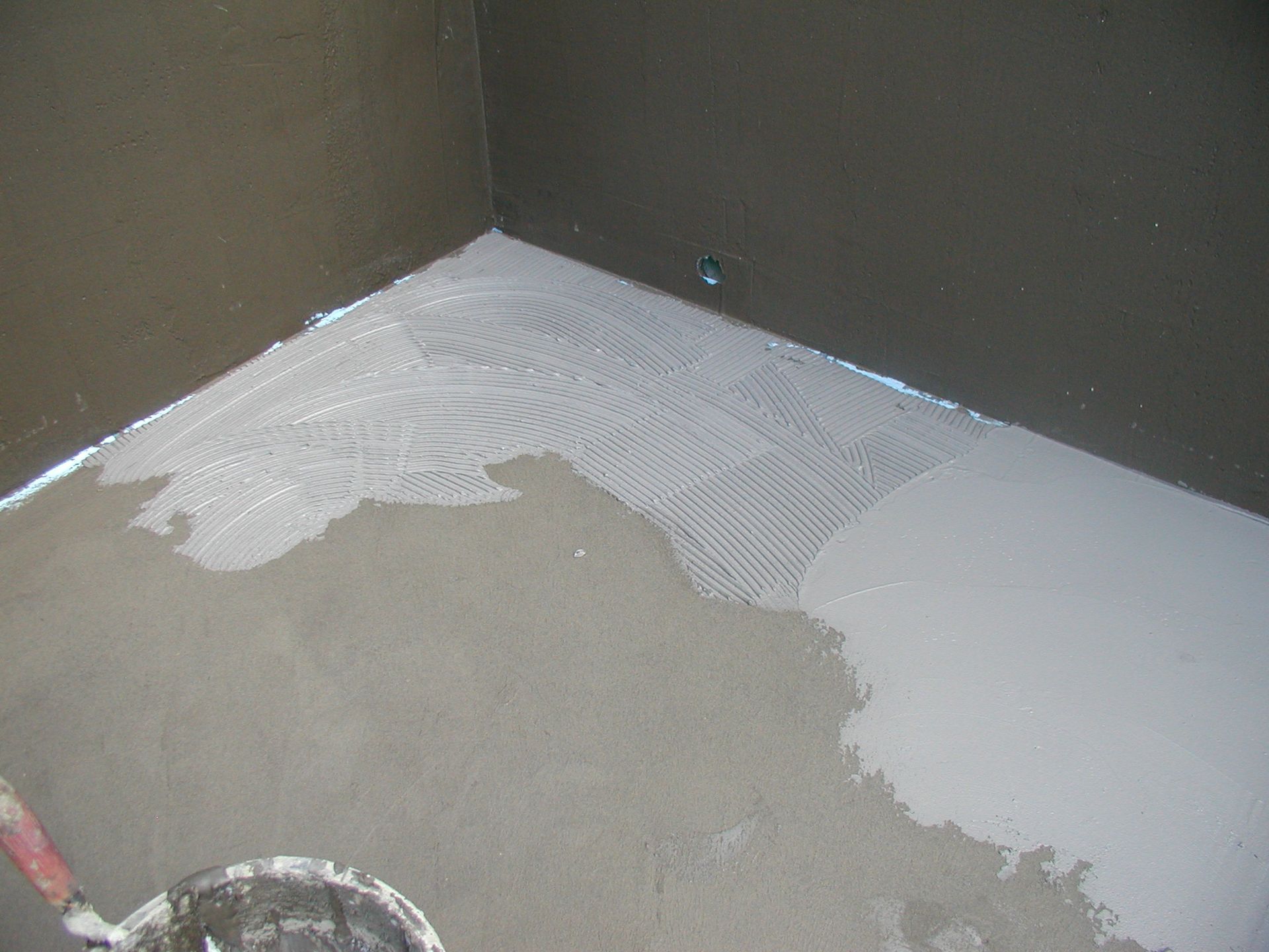 Grauer Badezimmerboden mit teilweise aufgetragenem weißem Klebstoff, in der Nähe einer Ecke.