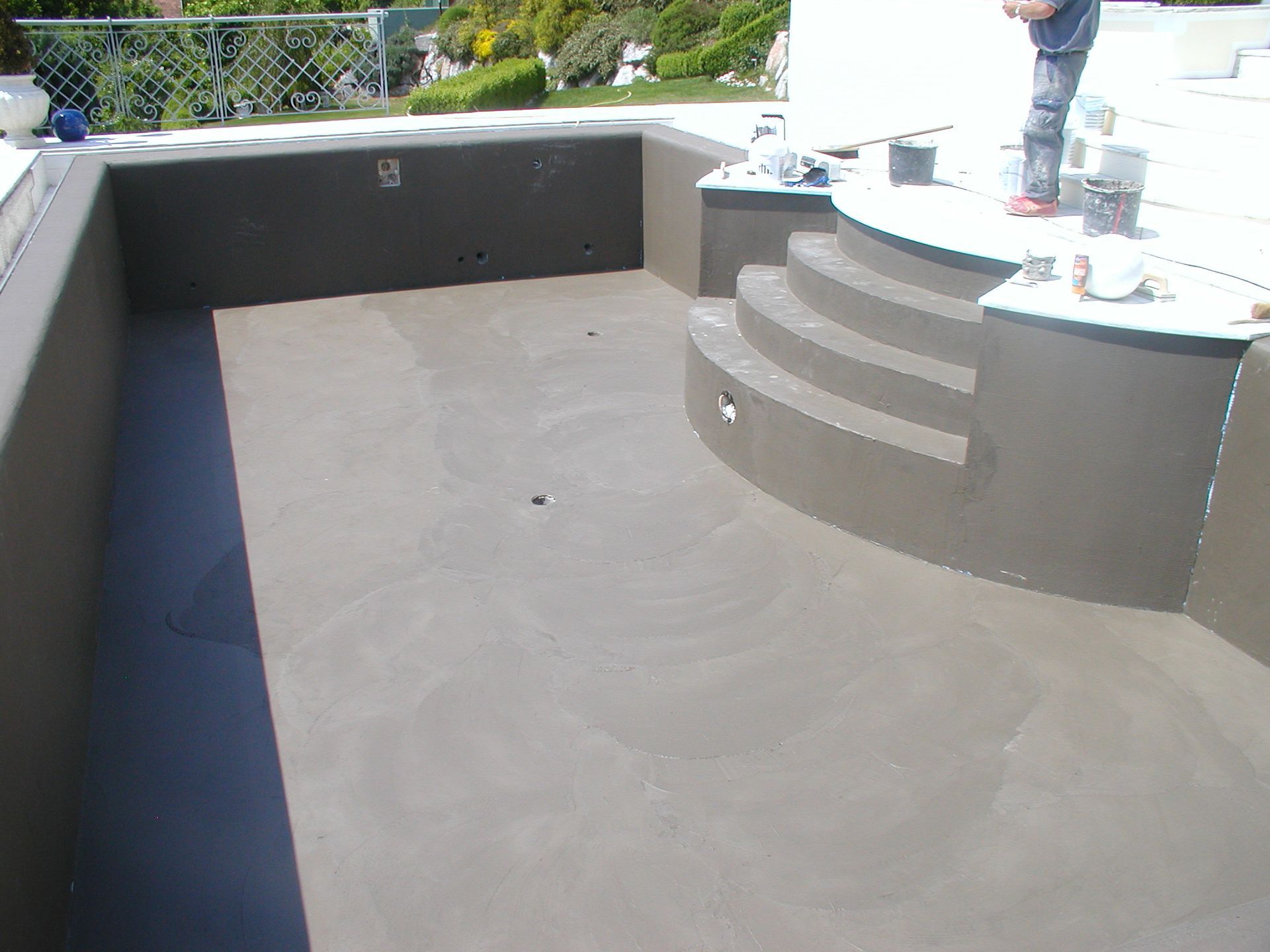 Ein leerer Swimmingpool mit dunklen Wänden im Bau. Eine Person steht in der Nähe auf dem Deck.