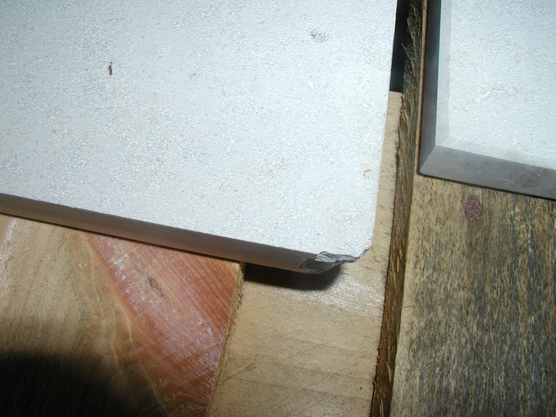 Nahaufnahme einer hellen Fliese mit beschädigter Kante, die auf Holzstützen ruht.